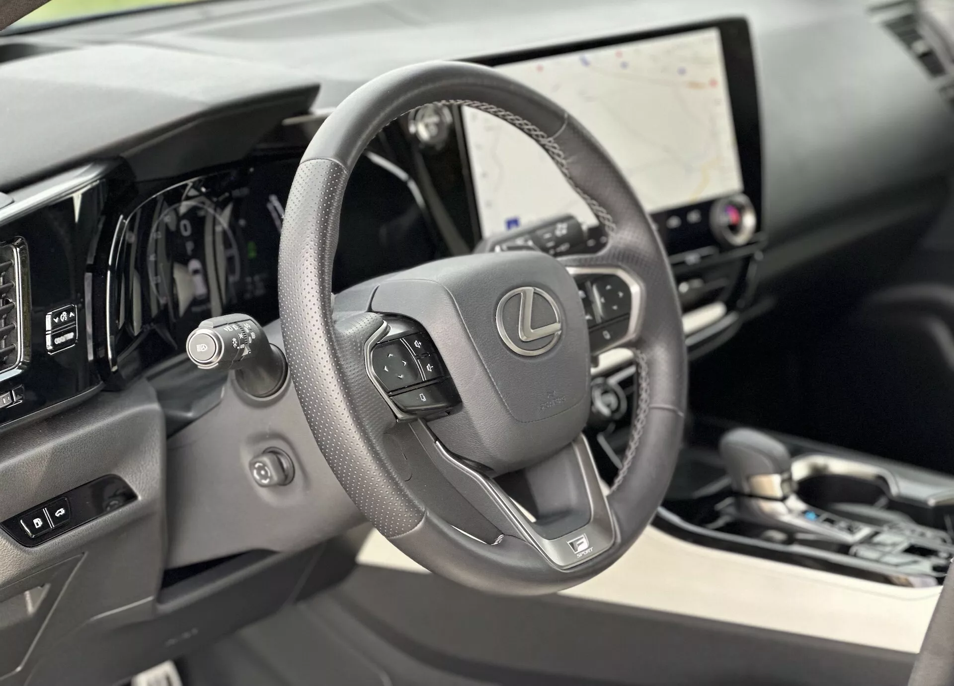 Vista interna del Lexus NX 2021 focalizzata sul volante rivestito in pelle con comandi integrati e cruscotto digitale dietro di esso, con grande touchscreen per l'infotainment e sottili accenni di lusso nei materiali di alta qualità