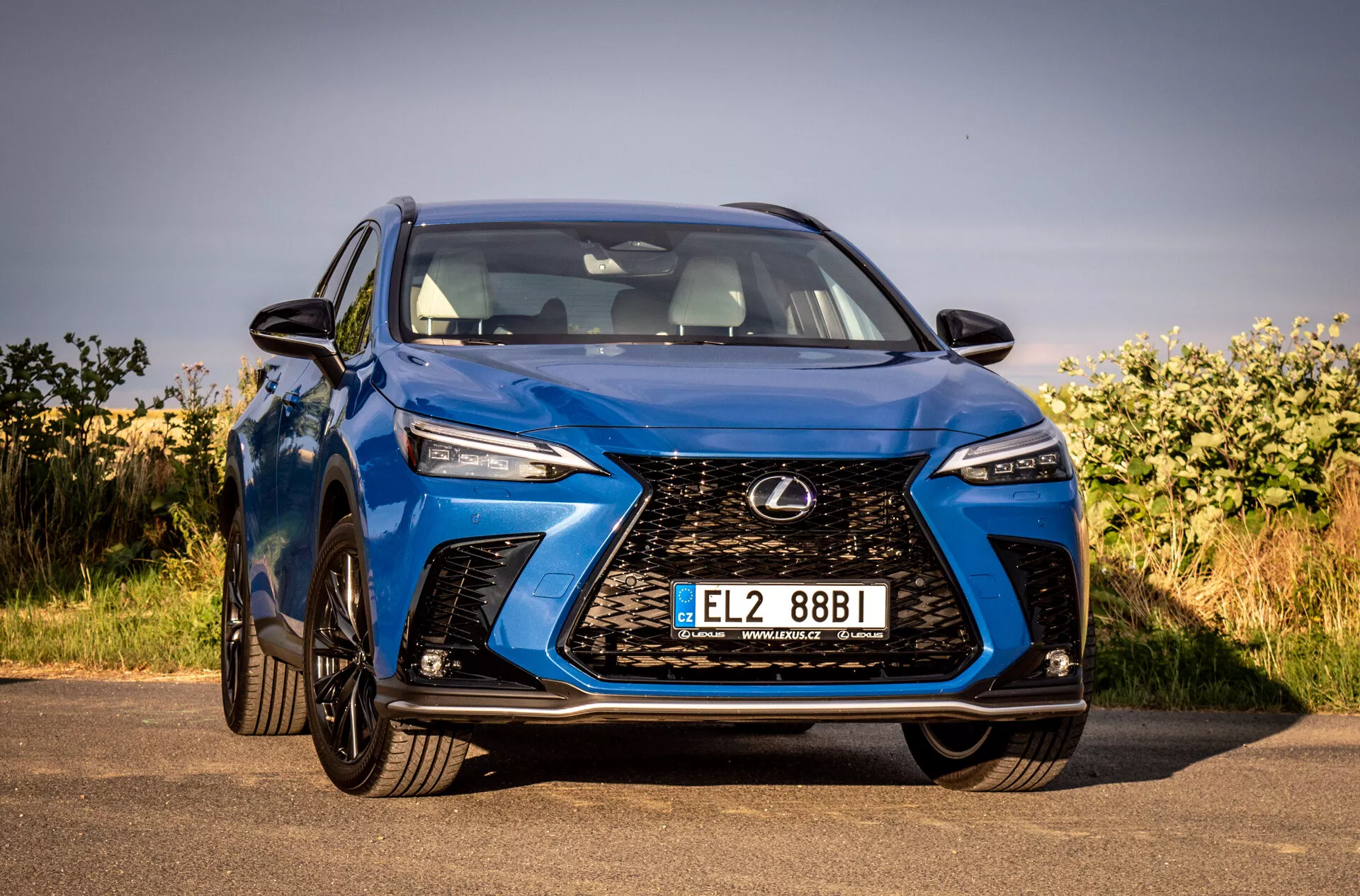 Vista angolare frontale di un SUV Lexus NX 2021 blu che mette in evidenza la sua griglia a fuso intricata, fari LED angolari, finitura lucida e design aerodinamico, parcheggiato all'aperto sotto cieli sereni