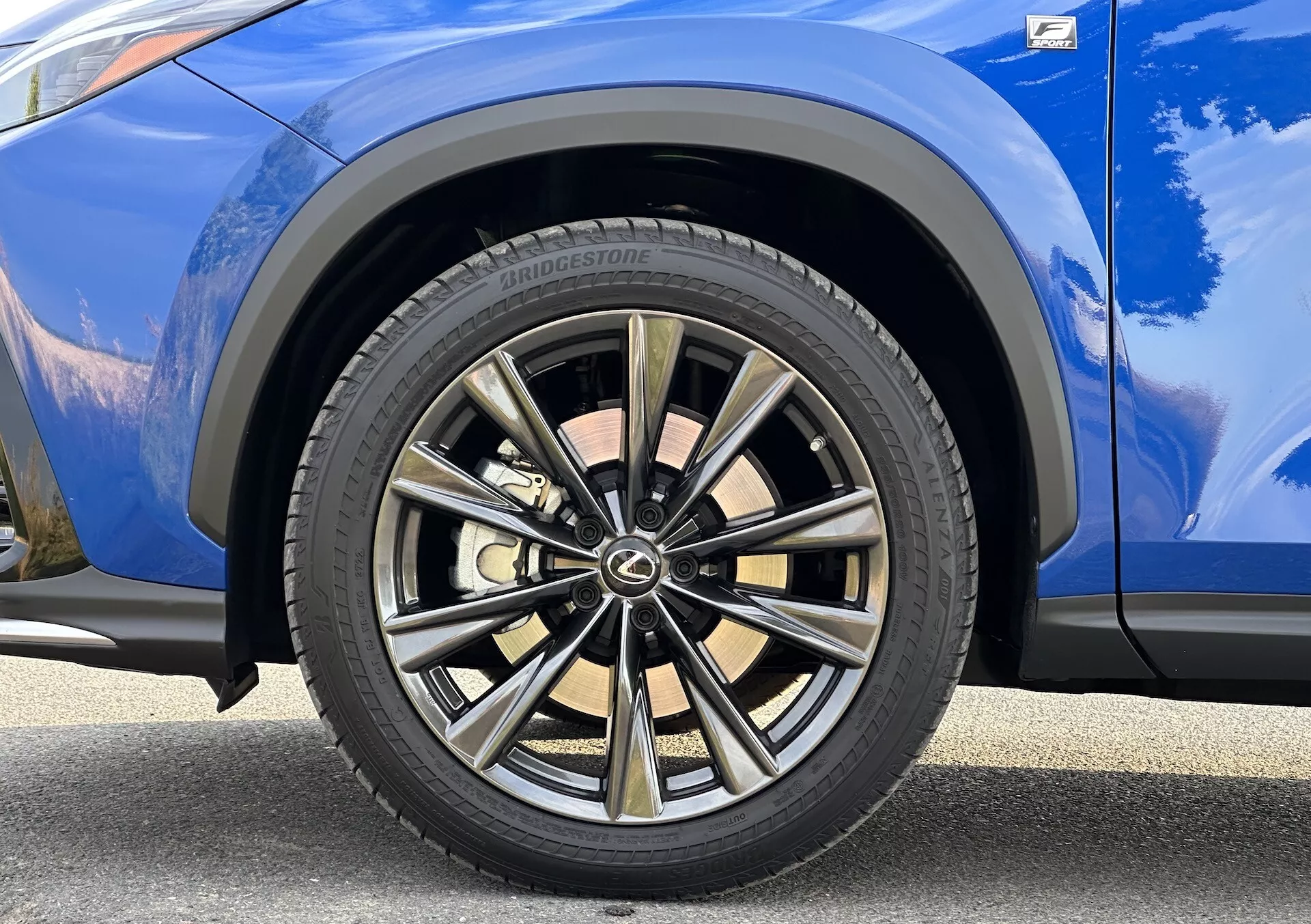 Vista dettagliata della ruota anteriore lato passeggero della Lexus NX 2021 con design a più razze con finitura bicolore e pneumatico Bridgestone, su carrozzeria blu vibrante