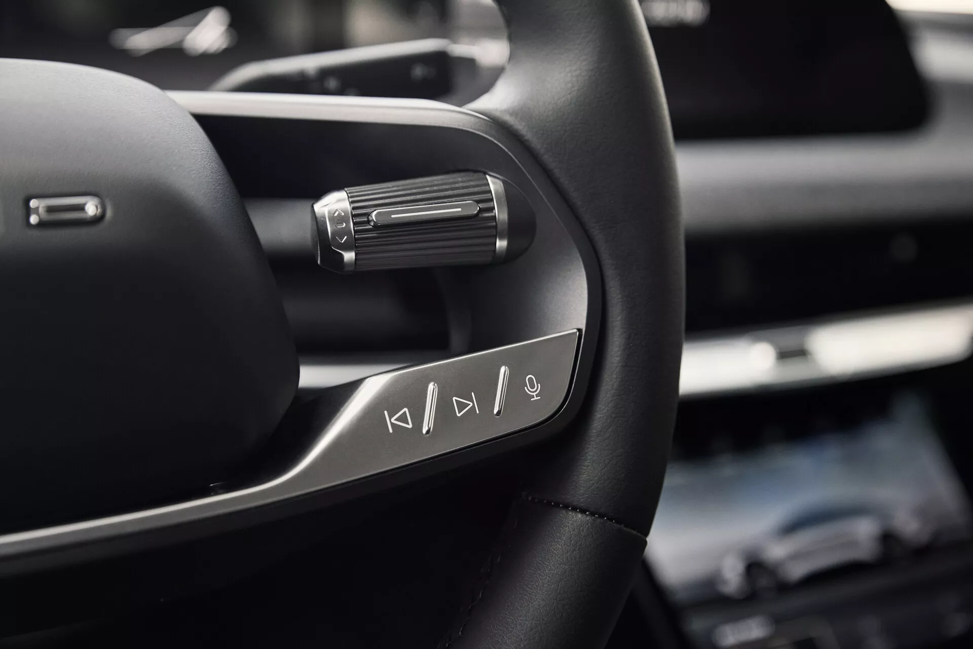 Vista ravvicinata del lato sinistro del volante del Lucid Air 2022, che mostra i pulsanti di controllo multimediale multifunzionali. La foto, scattata da sotto il volante all'altezza del petto di un conducente seduto, evidenzia il materiale in pelle di alta qualità con accenti metallici e una paletta dietro il volante, che indica funzioni di guida avanzate.
