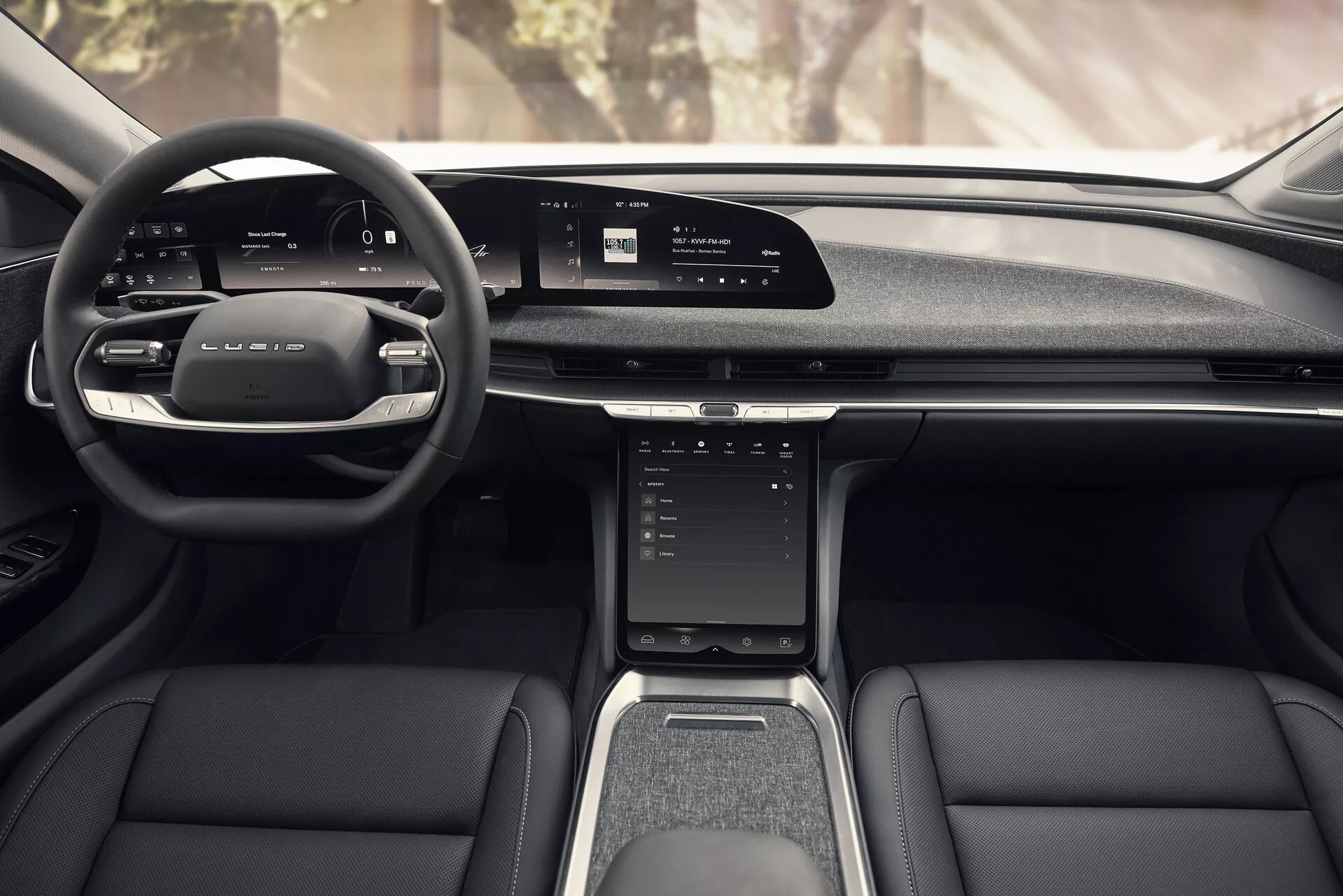 Vista dal sedile centrale posteriore dell'interno della Lucid Air 2022, con un design moderno con volante multifunzione in pelle, ampio display digitale sul cruscotto, touchscreen verticale sulla console centrale, palette di selezione marcia manuale, sedili anteriori eleganti in pelle e tessuto, tunnel centrale con leva del cambio e portabicchieri, e pannelli delle portiere con tasche portaoggetti e griglie degli altoparlanti.