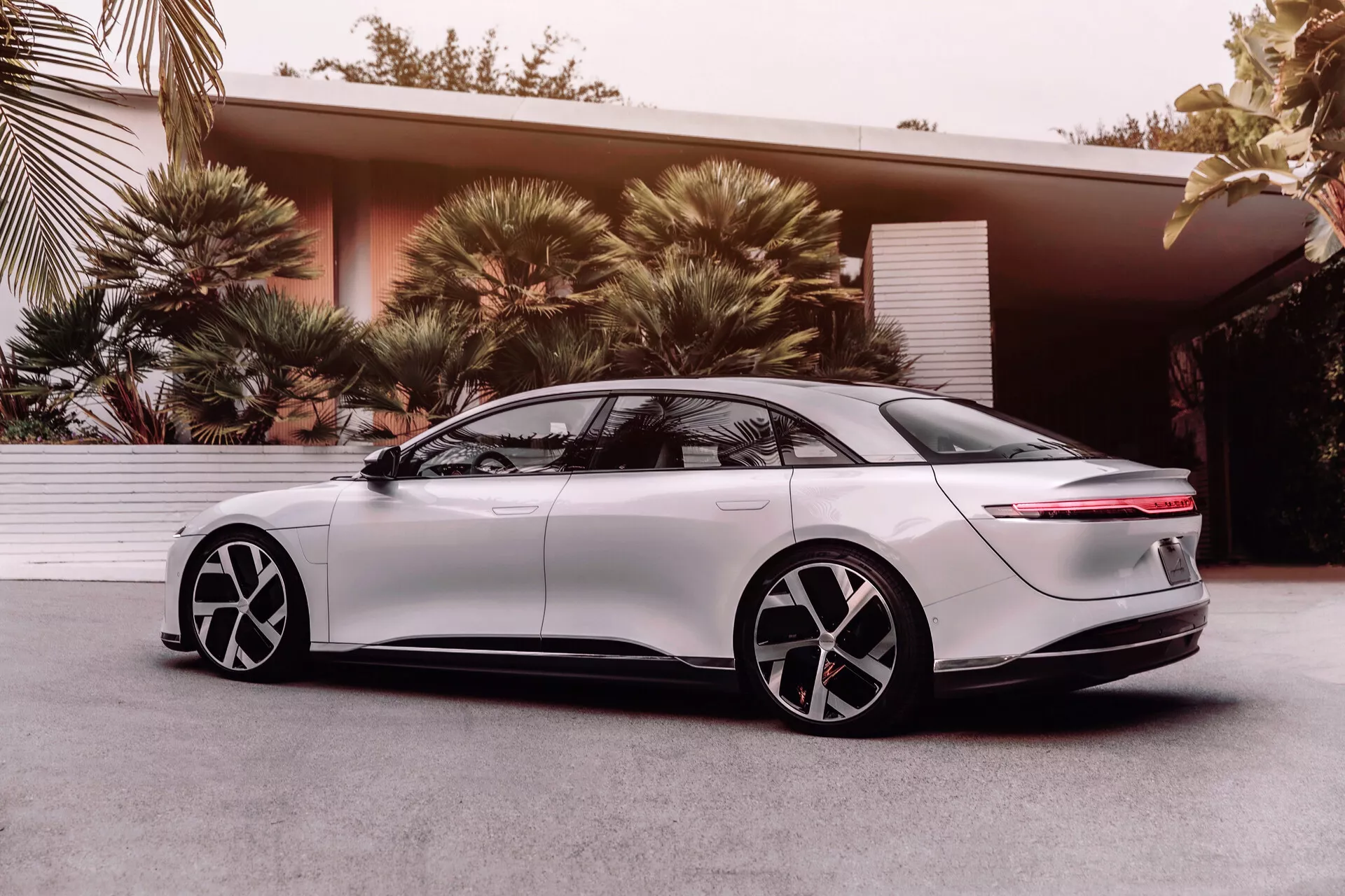 Lucid Air 2022 berlina elettrica, 1ª generazione, vista di profilo laterale da un angolo basso che enfatizza il design aerodinamico, fari a LED eleganti, parafango anteriore liscio, maniglie delle porte a filo retrattili, cerchi in lega a cinque razze bicolore, finestrini oscurati, posteriore fastback con barra luminosa orizzontale e spoiler integrato, che mostra la tecnologia e il design moderno dei veicoli elettrici.