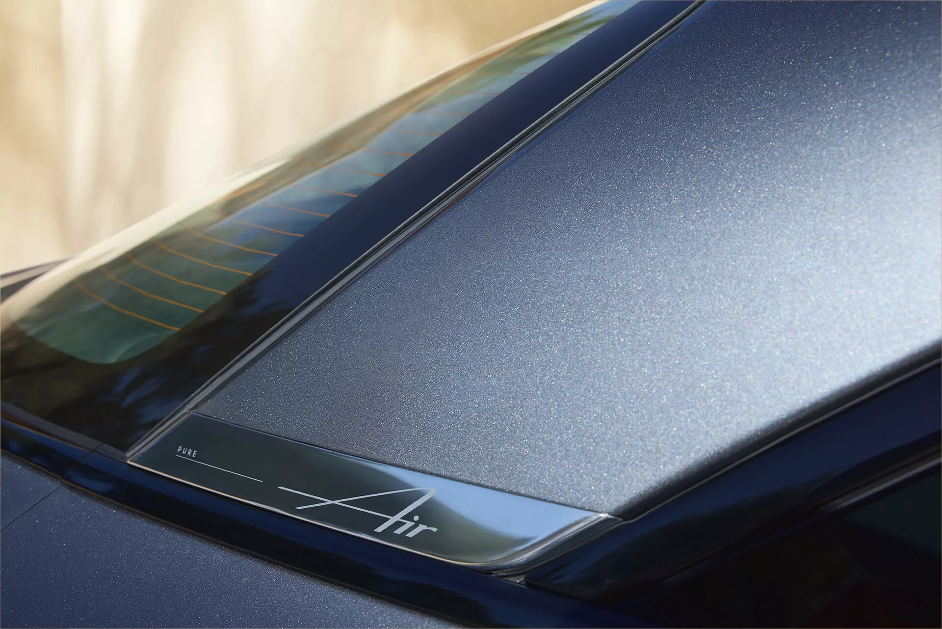 Primo piano della sezione posteriore vicino al tetto di una Lucid Air 2022 (1ª generazione), con un’evidente finitura lucida blu scuro e linee aerodinamiche eleganti. Presenta una striscia retroilluminata con l’inscrizione 'Air', che enfatizza il design di lusso e la possibile tecnologia avanzata.