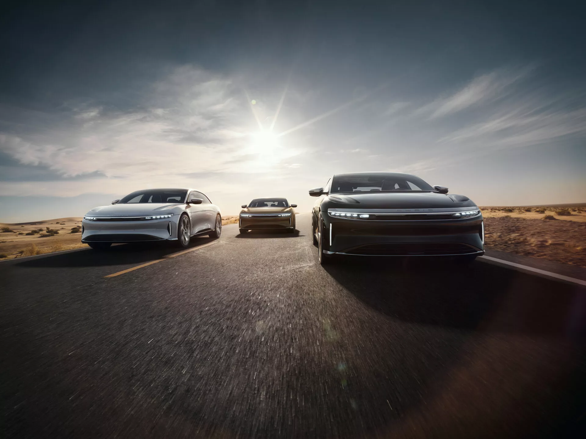 Vista frontale della Lucid Air 2022 con design aerodinamico e fari a LED in formazione a scalini su strada asfaltata con paesaggio desertico, luce solare che getta un bagliore caldo