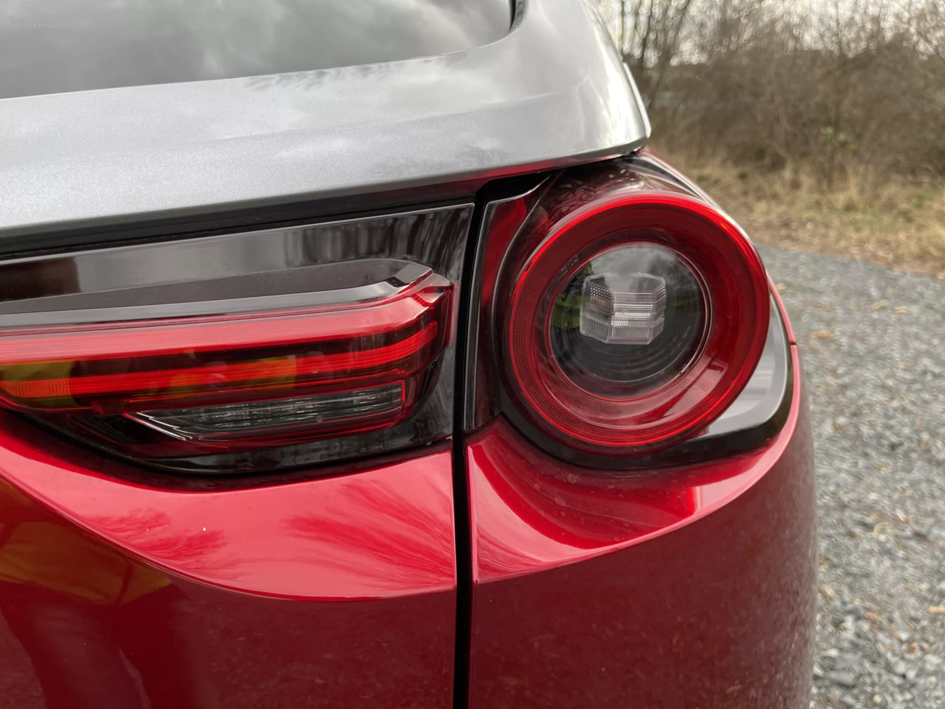 Vista ravvicinata dell'angolo posteriore di una Mazda MX-30 2020 che mostra il design dettagliato del fanale posteriore, vernice rossa lucida e riflessi sulla carrozzeria, evidenziando tecnologia di illuminazione e design dei veicoli moderni.