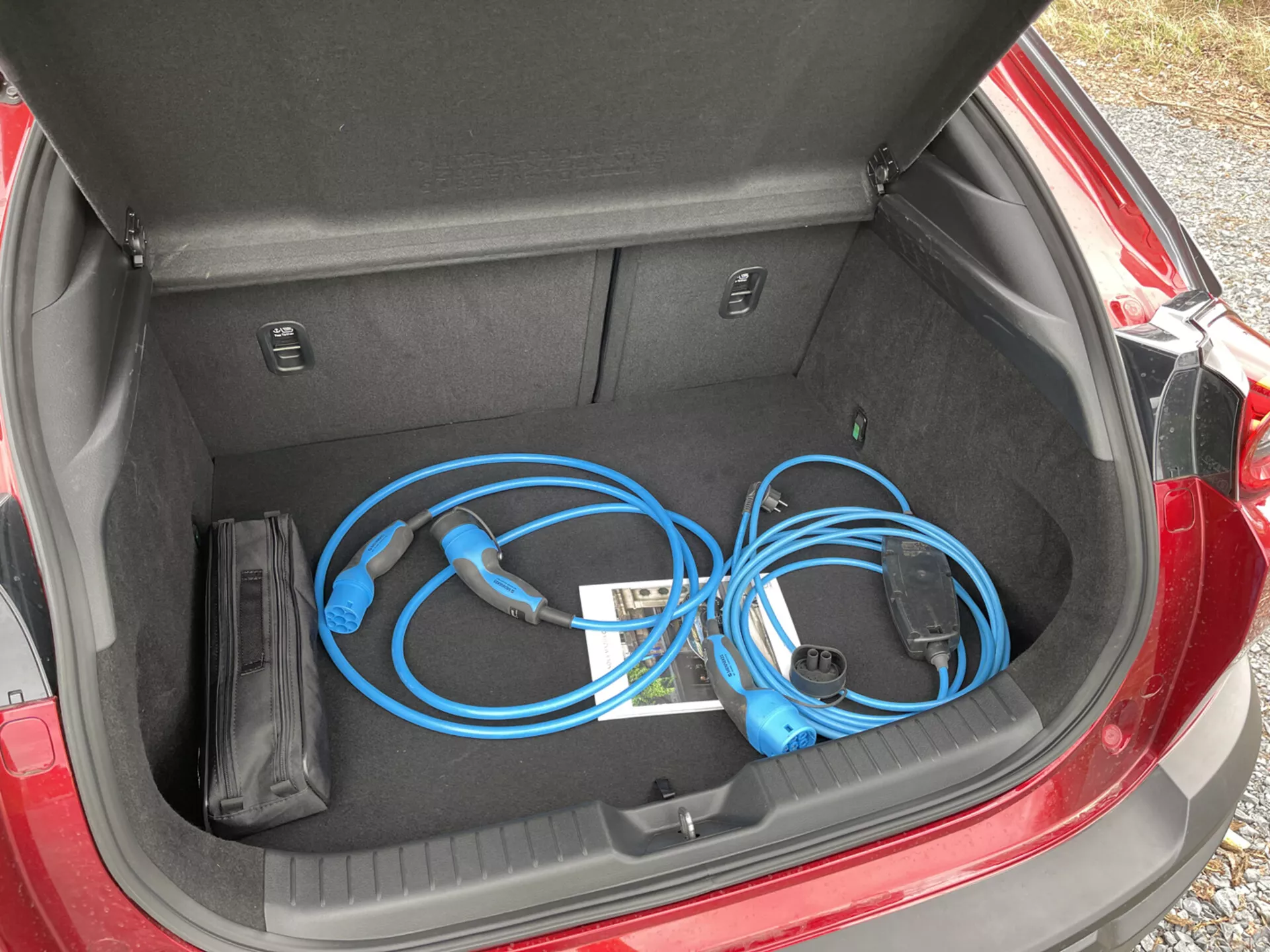 Baule aperto della Mazda MX-30 2020 che mostra un cavo di ricarica portatile per veicoli elettrici con vista ravvicinata dall'alto verso il basso da sinistra, esponendo lo spazio di stoccaggio pulito e piatto insieme ai compartimenti interni.