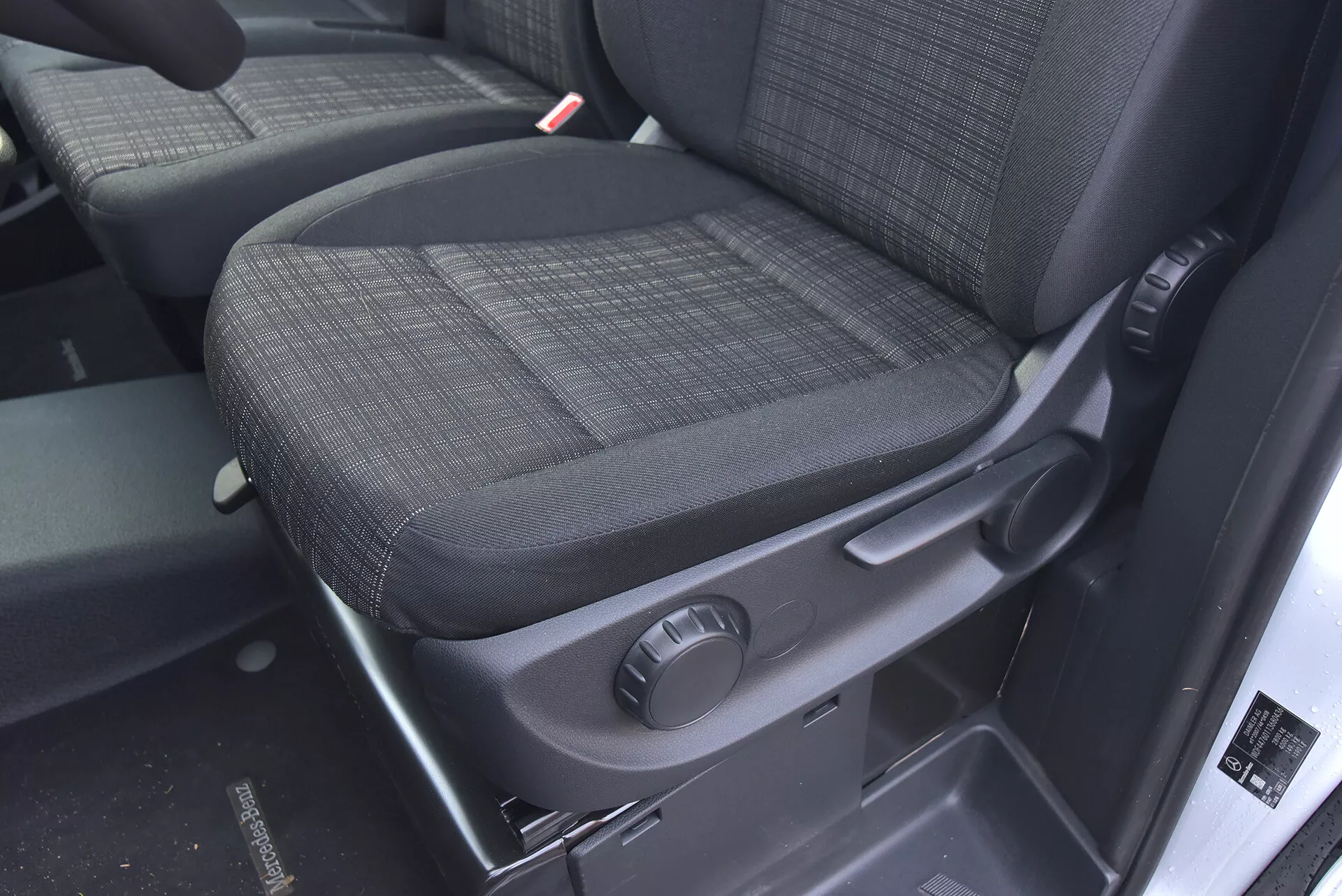 Interni Mercedes-Benz Vito 2014 Tourer con focus sul sedile del passeggero in tessuto scuro durevole, manopola per la regolazione manuale e caratteristiche di sicurezza come la chiara visibilità del ricevitore della cintura di sicurezza.