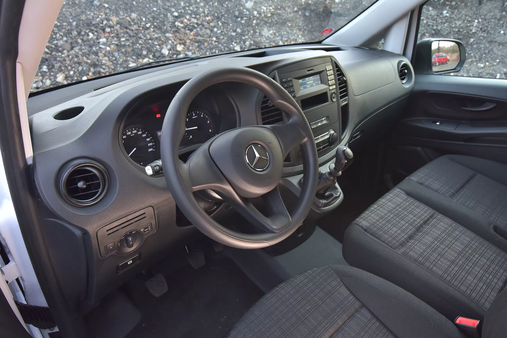 Interno del Mercedes-Benz Vito Tourer del 2014 visto dalla porta del conducente aperta, evidenziando il volante con logo Mercedes, il cruscotto, la consolle centrale, i sedili in tessuto, i controlli sulla porta e le bocchette d'aria.