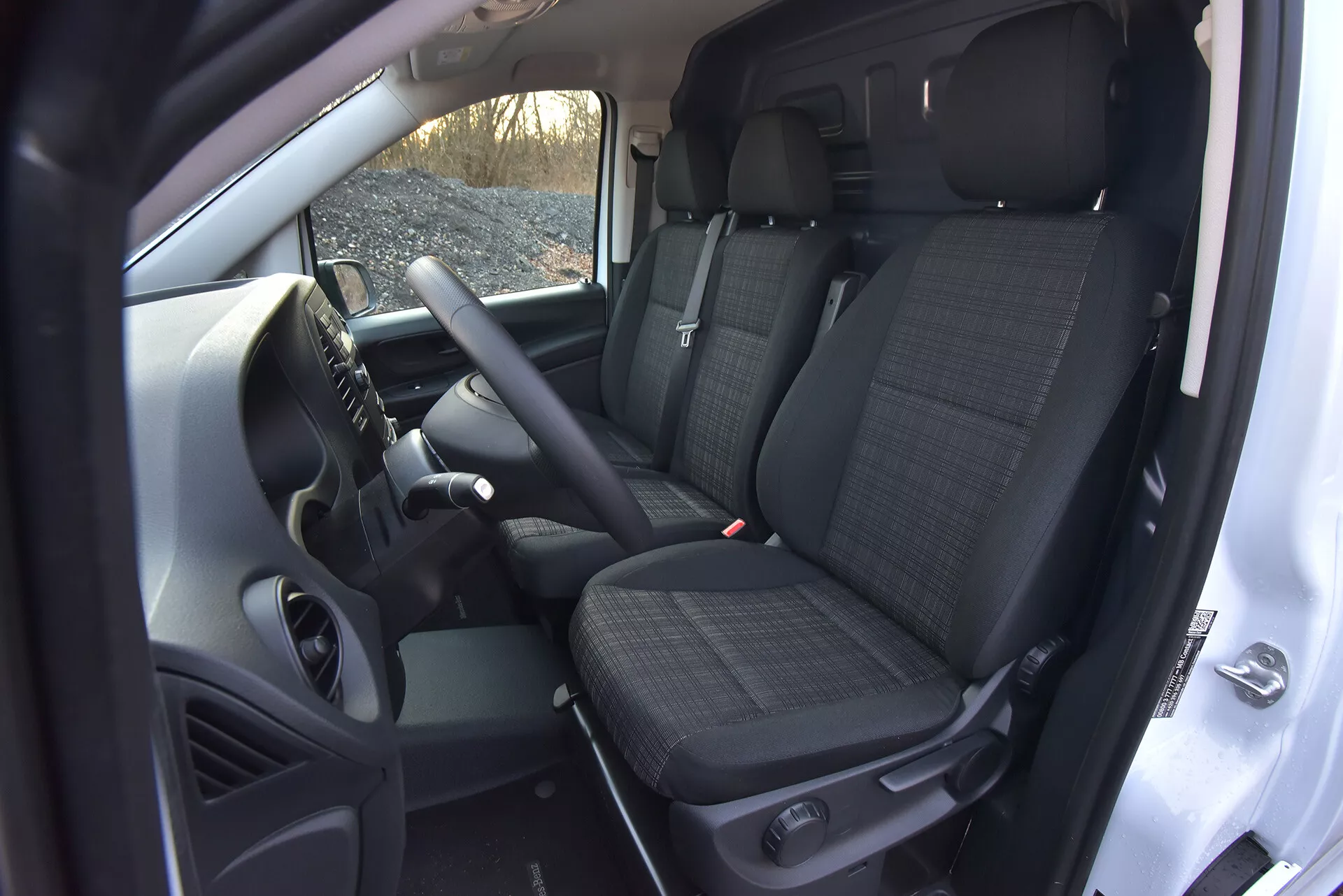 Vista interna del Mercedes-Benz Vito 2014 (Vito-Tourer) che mostra l'area del conducente e del passeggero anteriore con caratteristiche tecnologiche come comandi montati sul volante, una console centrale che potenzialmente ospita un sistema di infotainment, sedili anteriori con tessuto a motivo e poggiatesta, e uno scorcio dei sedili posteriori, tutto preso da un'angolazione elevata che evidenzia la spaziosità della cabina e gli elementi della trasmissione manuale.