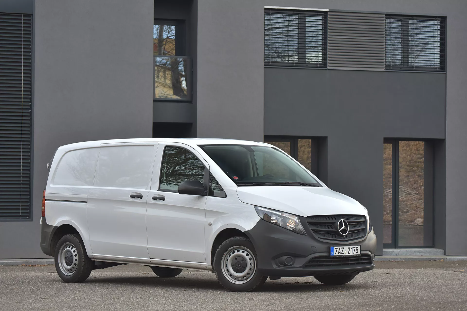 Furgone Mercedes-Benz Vito Tourer del 2014 di colore bianco parcheggiato su asfalto, mostrando profilo frontale e laterale con chiara vista del stemma sulla griglia e fari moderni, scattata con luce diurna nuvolosa davanti a un edificio minimalista