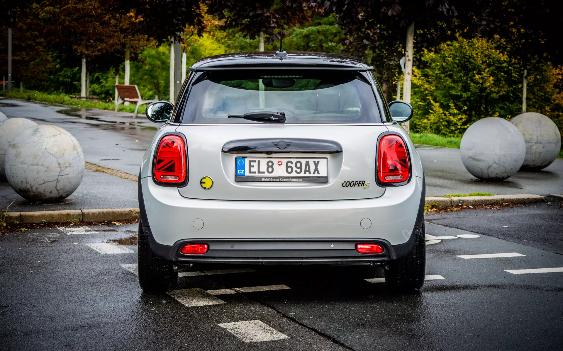 Vista posteriore di MINI Electric 3-Porte 2021 evidenziando luci posteriori distintive, cofano del bagagliaio con marchio COOPER, lunotto posteriore chiaro con tergicristallo, spoiler aerodinamico sul tetto, emblema e distintivi del produttore, paraurti posteriore con sensori di parcheggio, e vista parziale delle ruote posteriori in un parcheggio