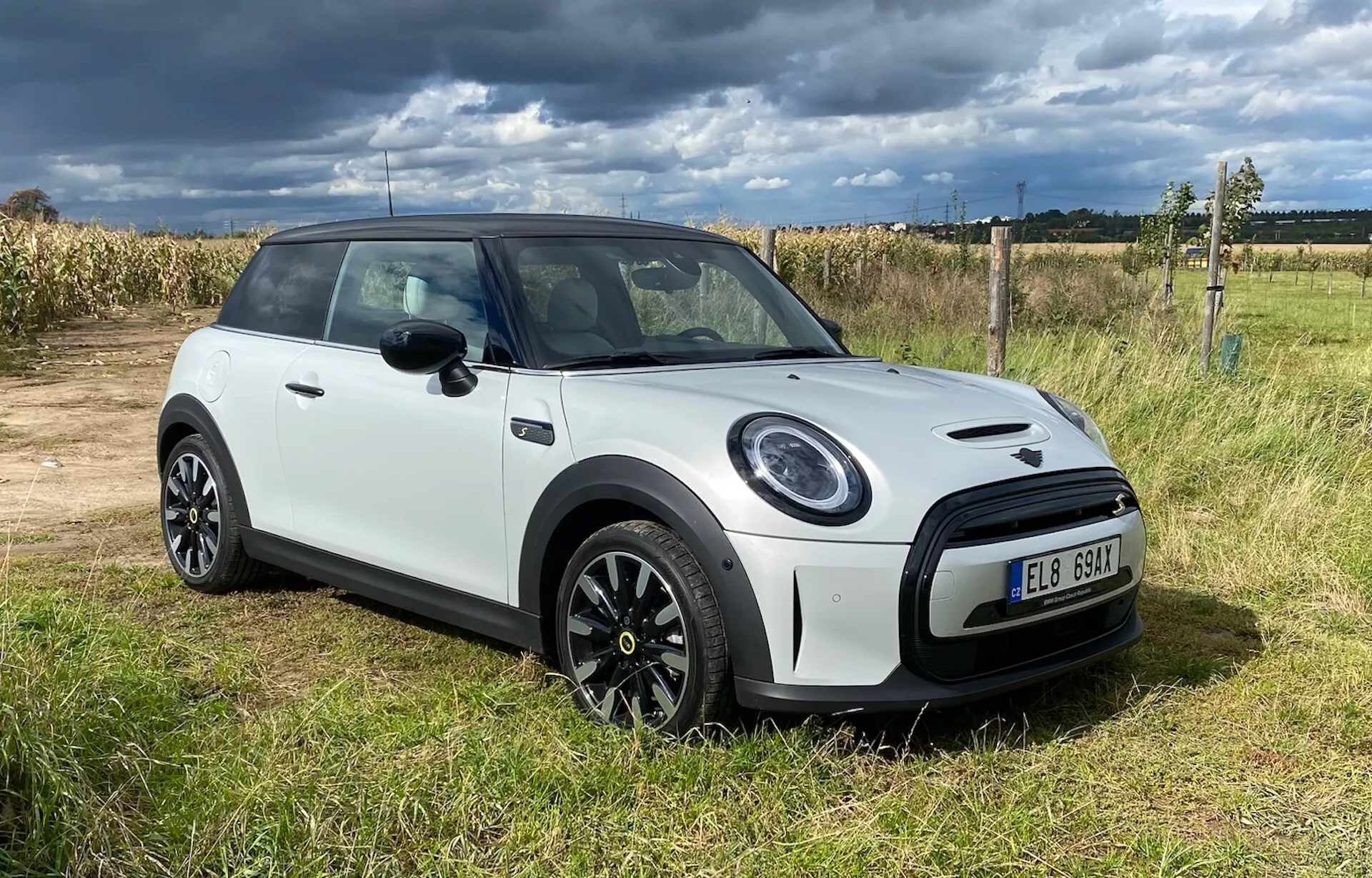 Modello Mini Cooper Elettrico 3 porte del 2021 in bianco, vista frontale inclinata su erba con cielo nuvoloso, mostrando bordatura nera personalizzata, fari rotondi, griglia esagonale e cerchi in lega a più razze