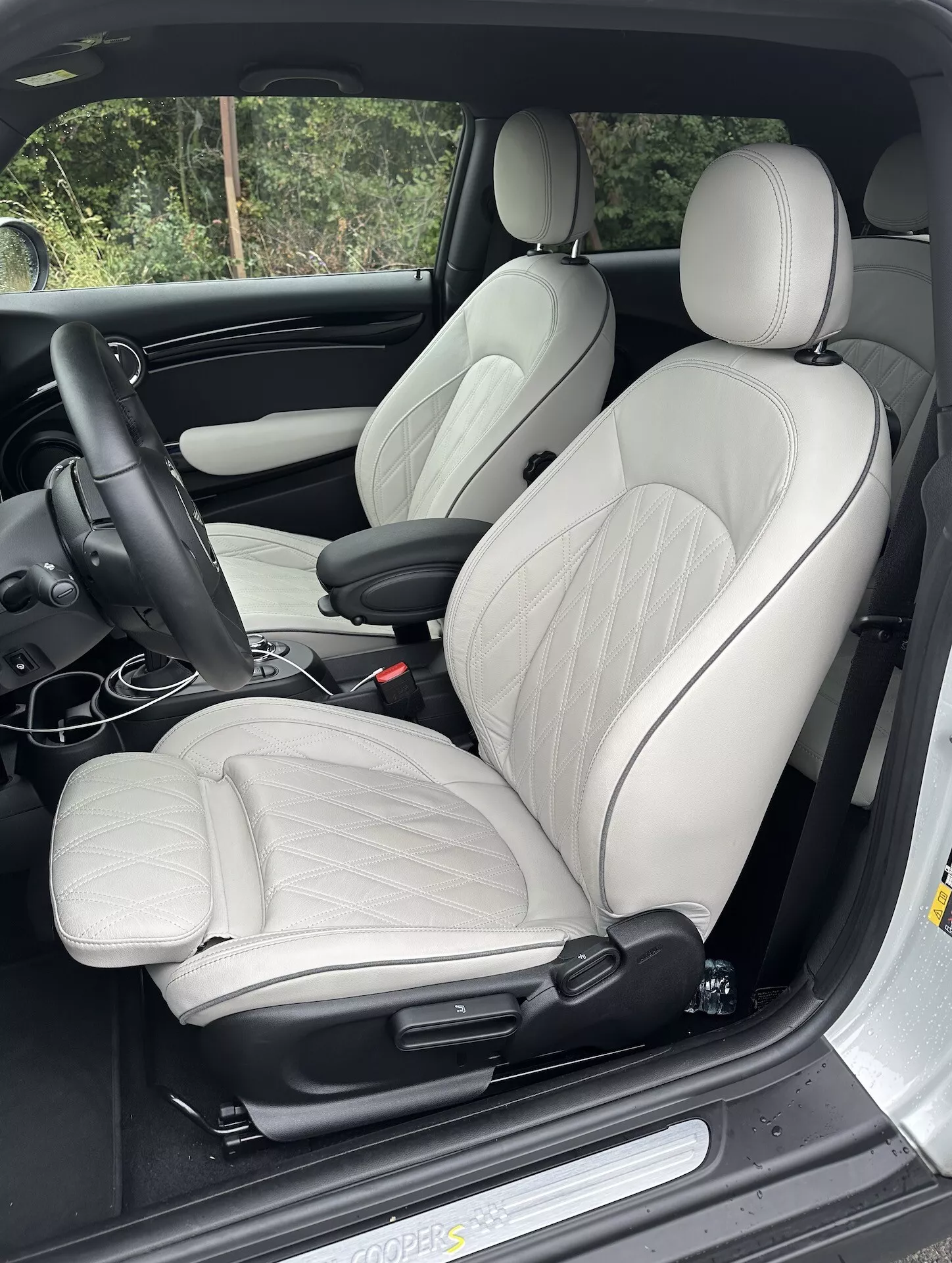 Vista interna del Mini Elettrico 3 Porte 2021 con focus sul sedile del conducente in pelle chiara, supporto laterale, e controlli per l'aggiustamento elettrico, impostato su cruscotto con guida a sinistra, che mostra elementi di lusso ergonomico e sportivi