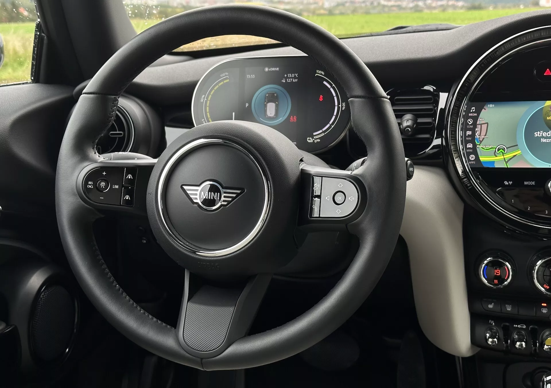 Vista interna della MINI Electric 3 Porte 2021 che mostra la cabina di guida dalla prospettiva del conducente, evidenziando il volante moderno a tre razze con pulsanti multifunzionali, quadro strumenti digitale e il sistema di infotainment con navigazione GPS sul cruscotto.
