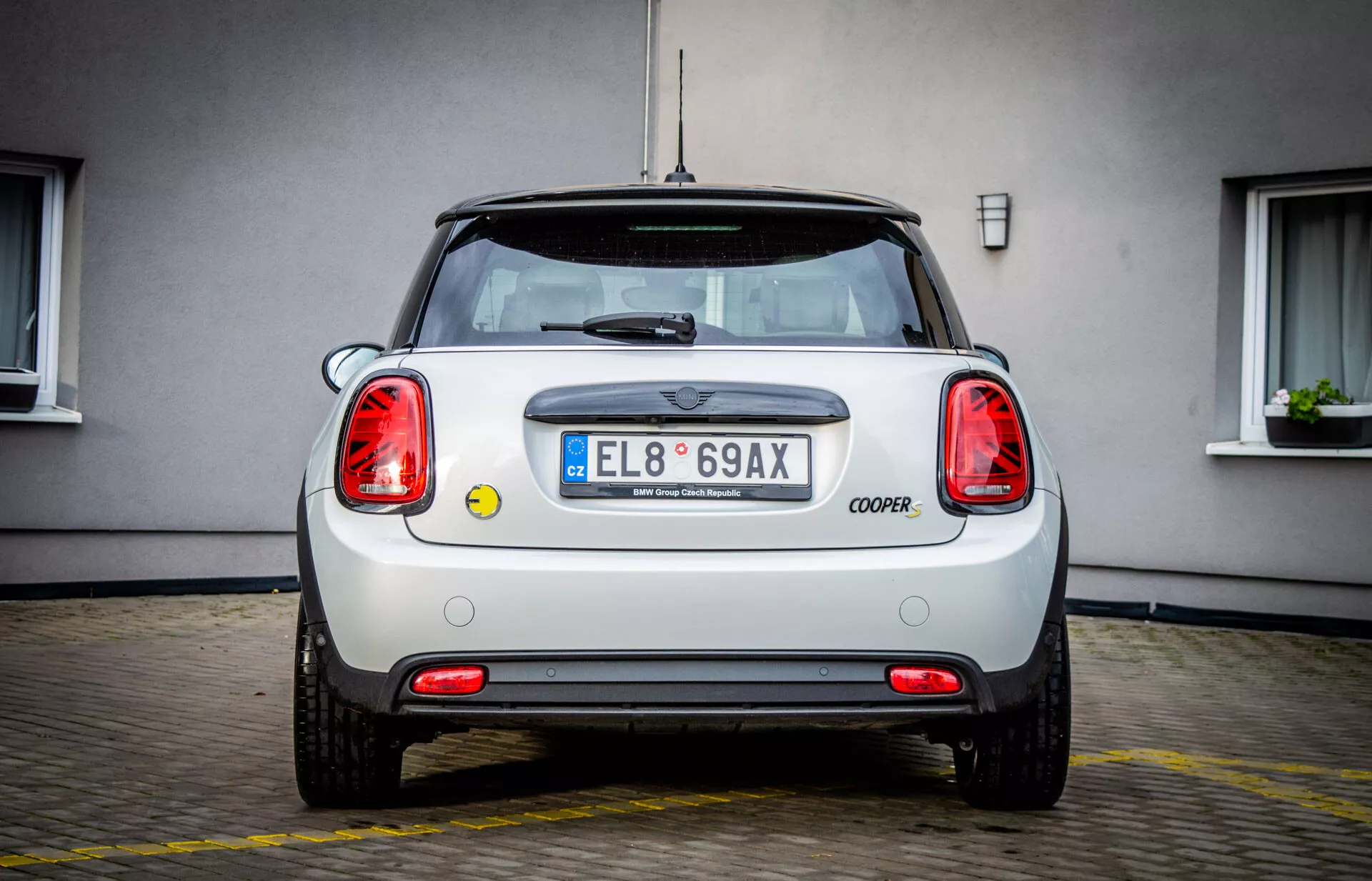 Vista posteriore di una Mini Electric 3-Door 2021 parcheggiata su cemento, con emblema, scritta COOPER, luci posteriori circolari, targa UE con 'E', paraurti in condizioni perfette con riflettori, sensori di parcheggio, uscita di scarico, schema di colore bicolore, antenna radio e lunotto posteriore con tergicristallo