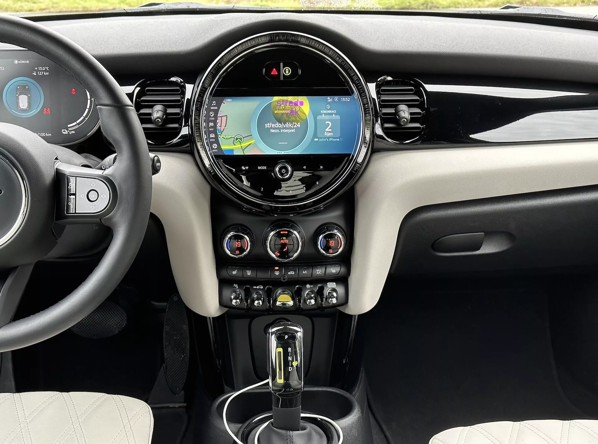 Interni del Mini Electric 3-Door 2021 che mostra il cruscotto anteriore, display digitale del cruscotto con navigazione, sistema di infotainment touchscreen centrale circolare, interruttori per il controllo del clima e leva del cambio automatica