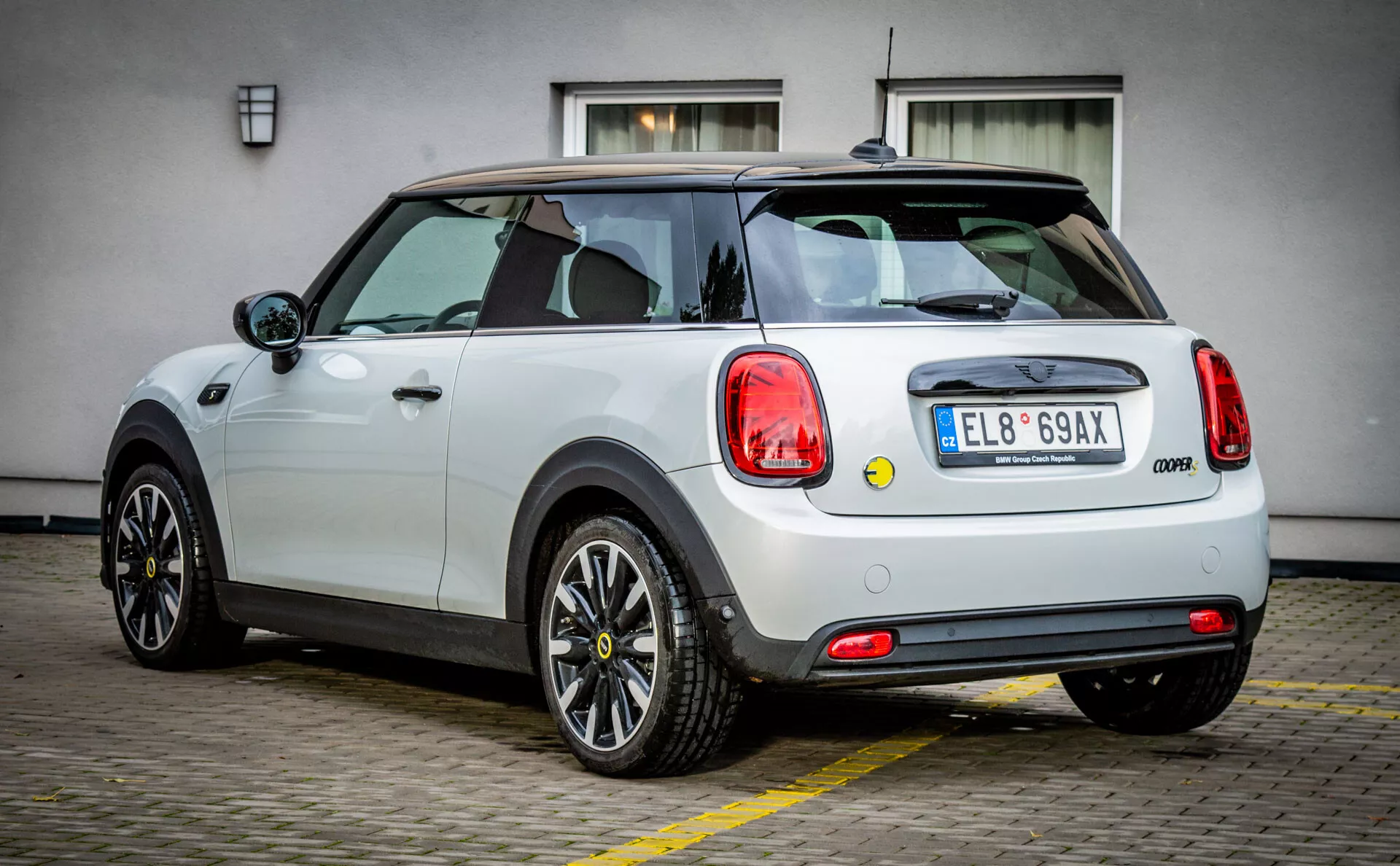 Mini Cooper moderna 2021 Electric 3-Door Hatchback bianca con tetto nero, cerchi in lega a più razze, finestrini senza telaio e sensori di parcheggio avanzati da un'angolazione posteriore di tre quarti che mostra il suo design e le sue caratteristiche.
