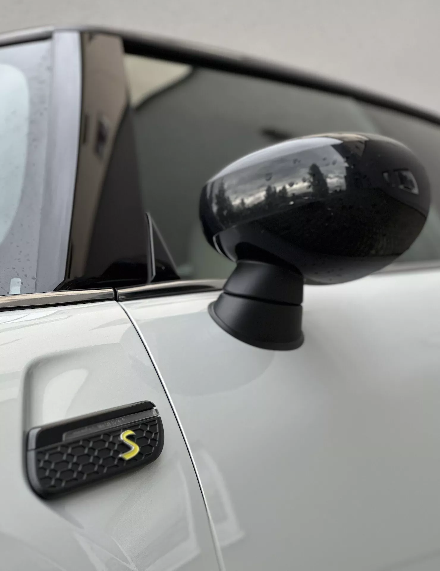 Vista ravvicinata dello specchietto laterale e del parafango anteriore della Mini Electric 3-Door con un design nero elegante e un emblema stilizzato 'S', sottolineando l'estetica moderna del veicolo e la tecnologia.