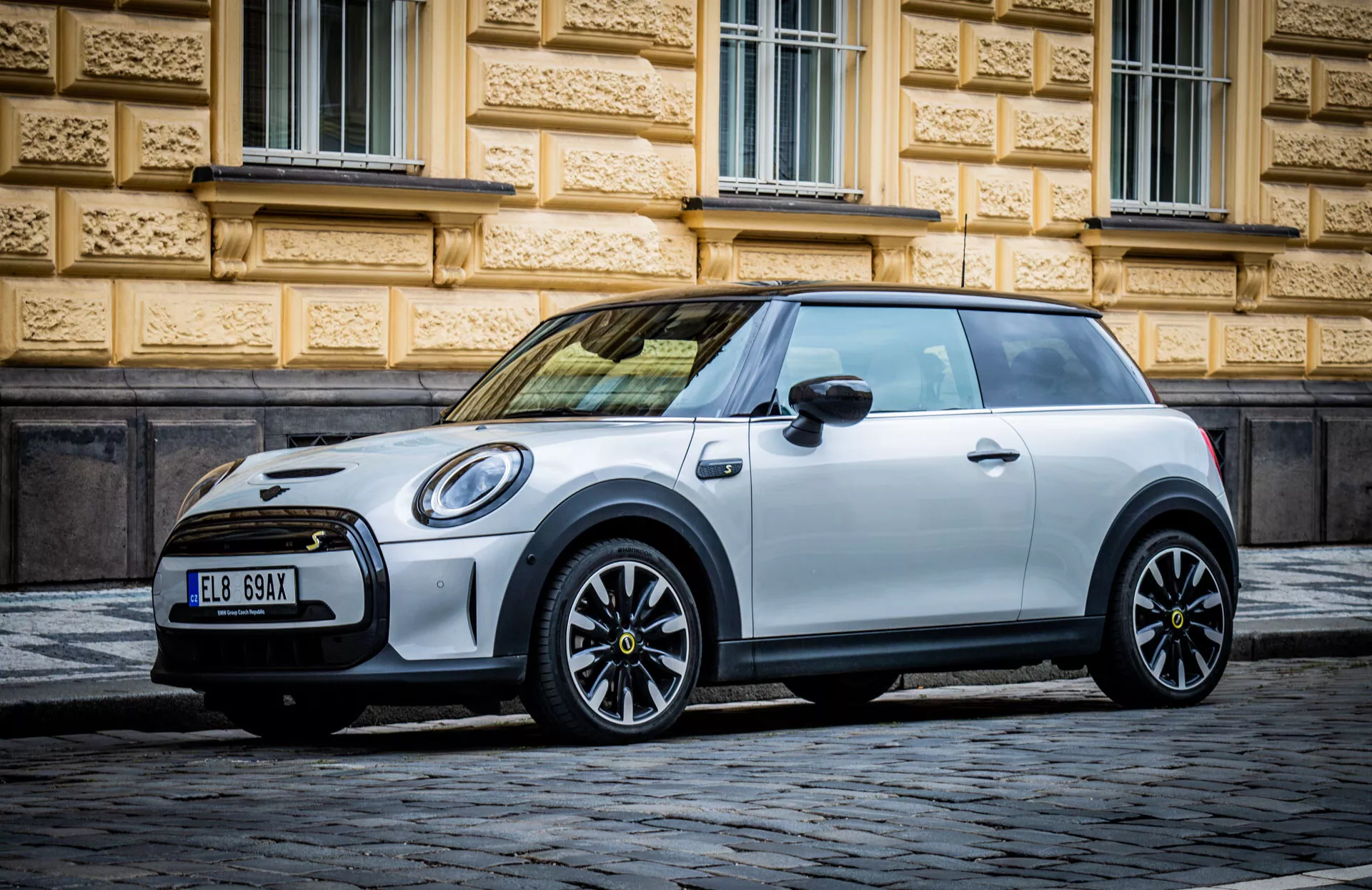 Mini Elettrica 3 porte hatchback del 2021 parcheggiata su una strada in ciottoli, mostrando un profilo laterale con enfasi sulle ruote in lega e sul design snodato e curvilineo caratteristico delle Mini, in condizioni di luce favorevoli
