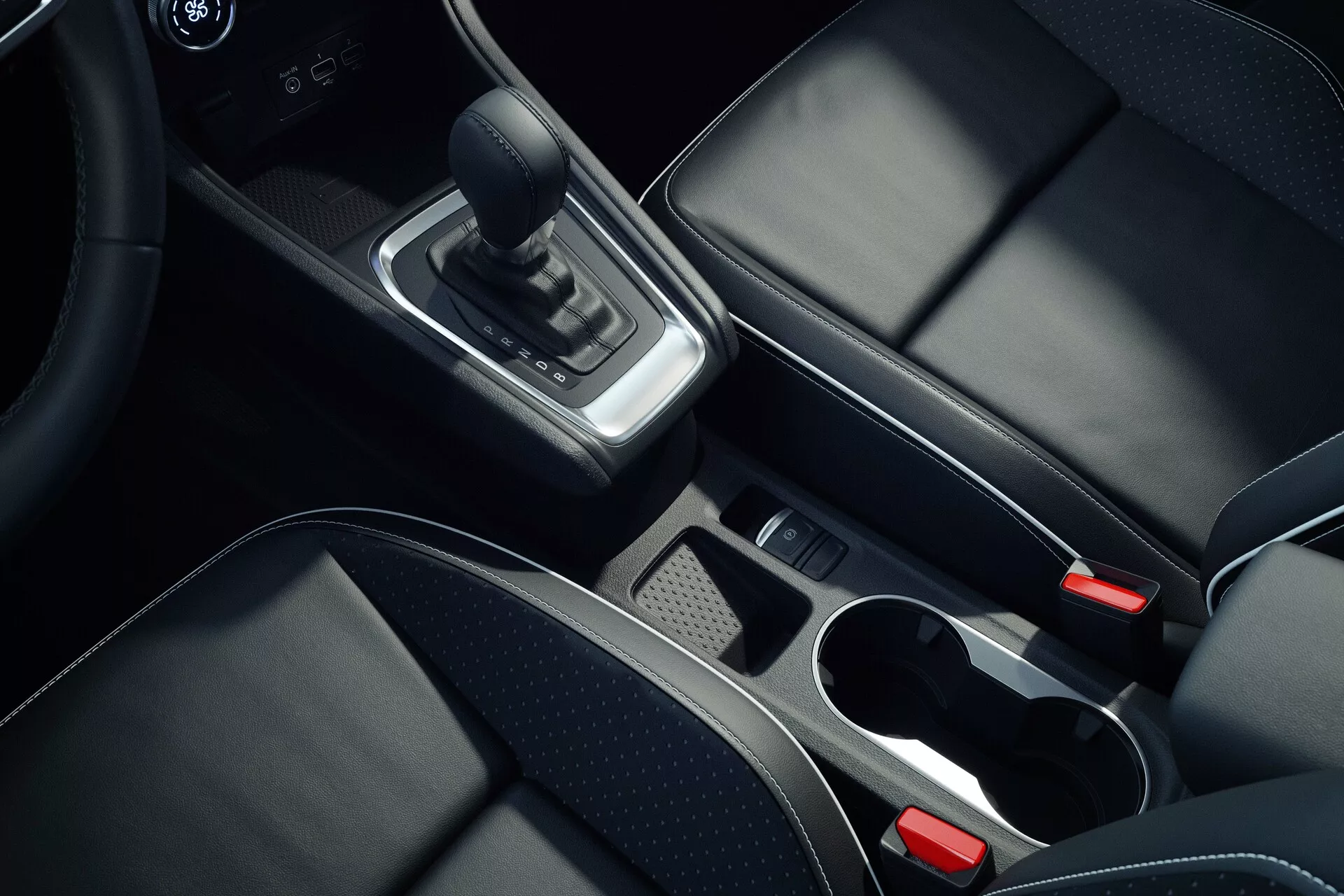 Scatto degli interni della console centrale della Mitsubishi ASX 2023 seconda generazione, ripreso da un angolo dall'alto, concentrandosi su dettagli come la leva del cambio in pelle, accenti cromati intorno all'area del cambio, vano portaoggetti con vassoio rimovibile, due portabicchieri con bordi cromati, sedili in pelle nera con cuciture visibili, pulsante del freno di parkeer elettronico e bracciolo centrale parzialmente visibile, mostrando materiali di alta qualità e design moderno.