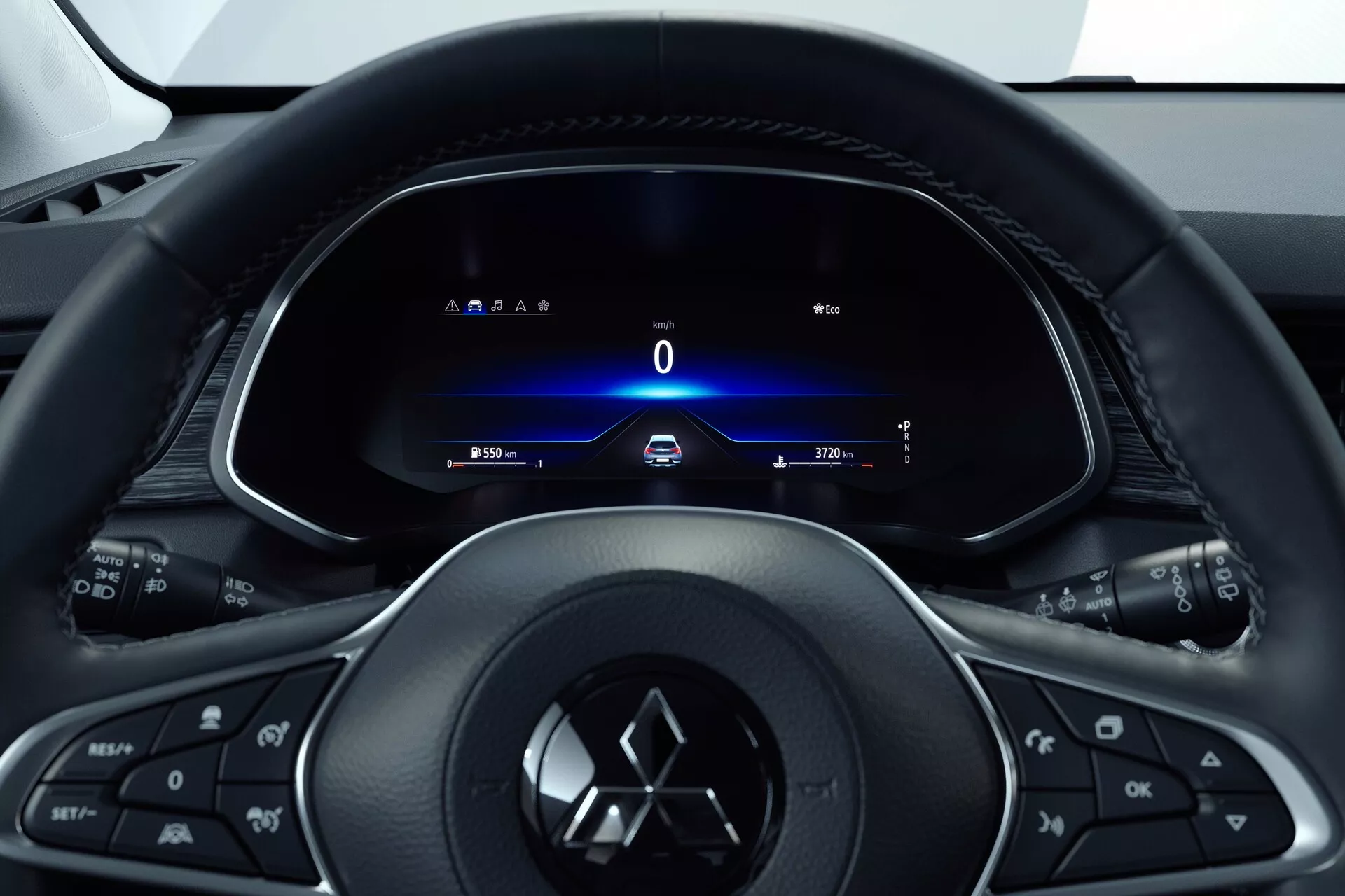 Vista interna della Mitsubishi ASX 2023 (2ª generazione) dal sedile del conducente, focalizzata sul volante multifunzione a tre razze con pulsanti per media, telefono, controllo della velocità e con il logo del produttore. Dietro, un quadro strumenti completamente digitale mostra un velocimetro a 0 km/h, indicatori di direzione, orario e contachilometri. Il design in stile cockpit indica un approccio orientato al conducente con un'estetica elegante e moderna che mette in risalto la tecnologia e il facile accesso alle informazioni e ai comandi del veicolo.