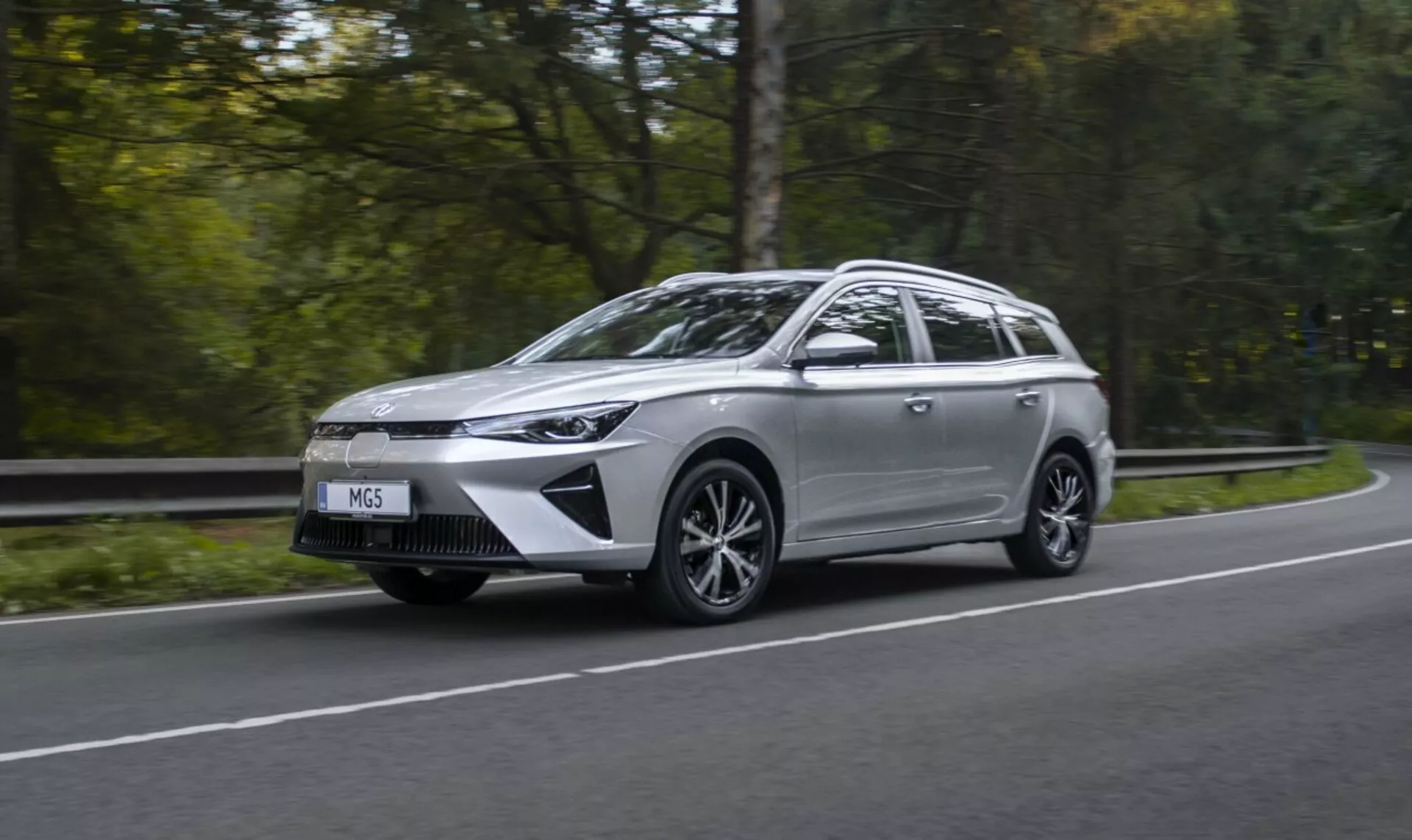 Mitsubishi Outlander Plug-In Hybrid 2018 in movimento su una strada circondata da alberi, mostrando il suo design elegante e i fari LED, con uno sfondo verde sfocato che enfatizza velocità e tecnologia ecologica.