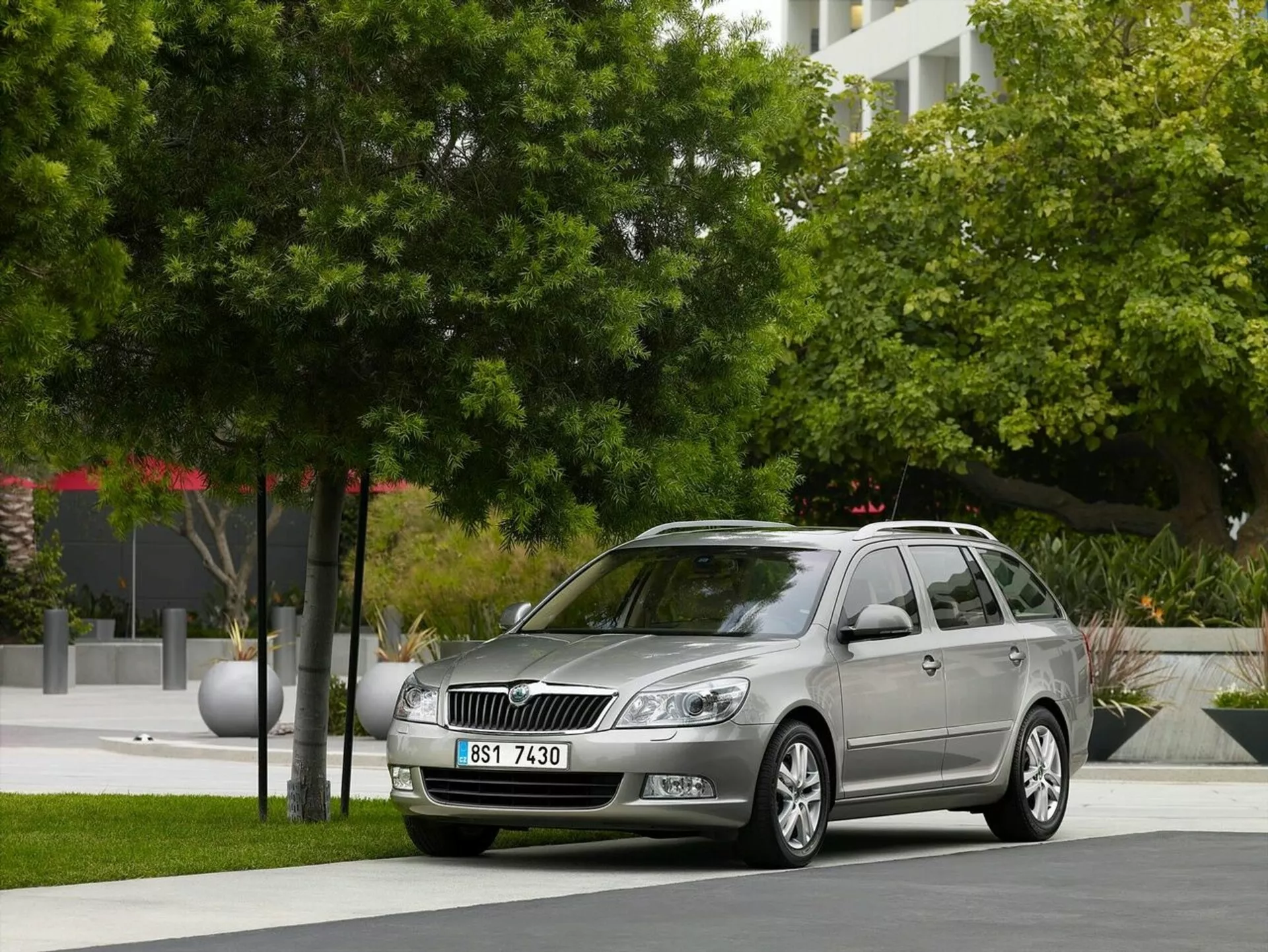 Station wagon Opel Astra del 2011 parcheggiata in un contesto urbano con verde e edifici moderni sullo sfondo, mostrando la griglia frontale dell'auto, i fari e un profilo laterale elegante incluso cerchi in lega e barre sul tetto