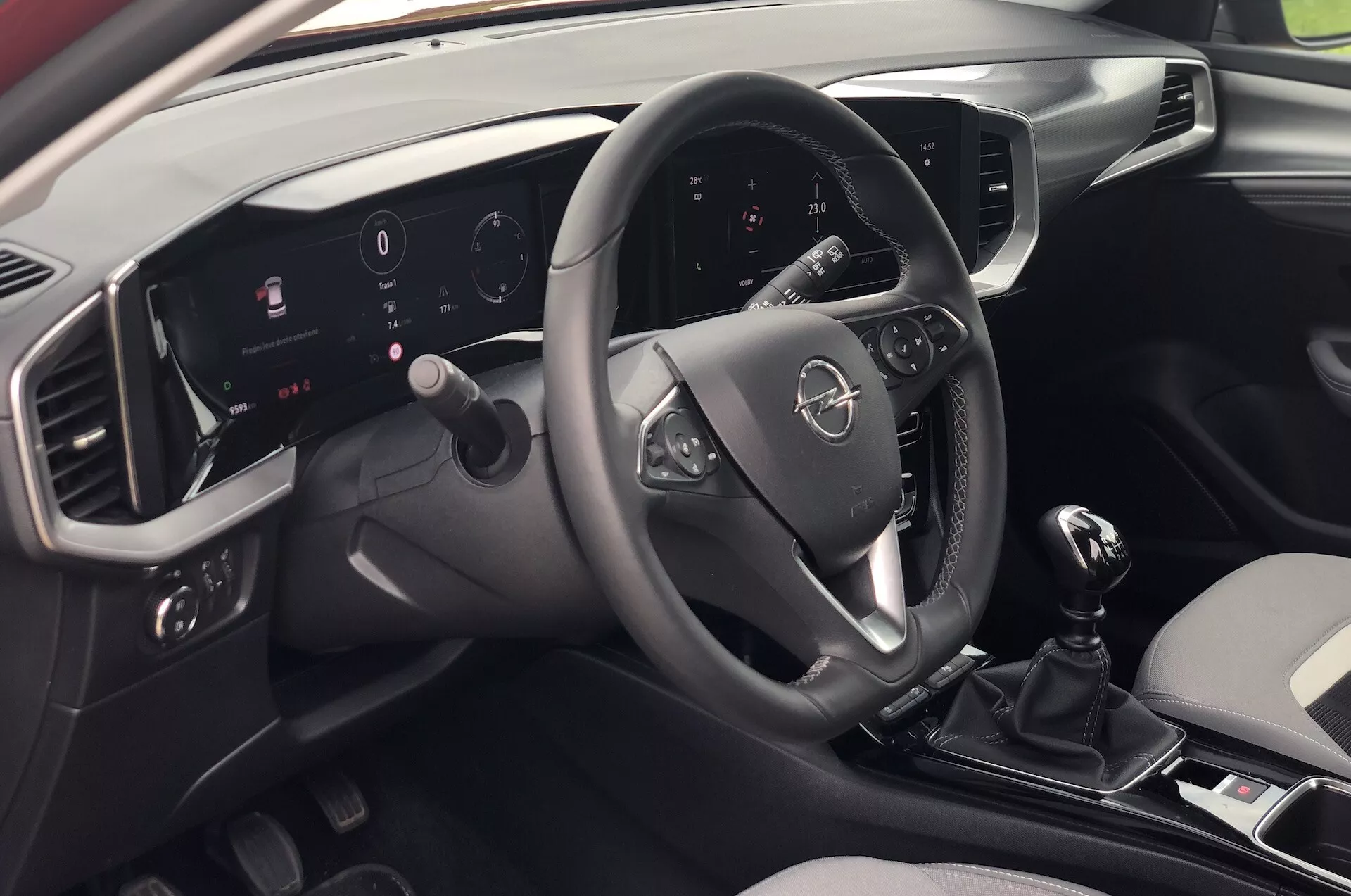 Vista degli interni della Opel Mokka 2021 dalla prospettiva di un passeggero seduto dietro a destra, che mostra il moderno cruscotto, volante multifunzione, quadro strumenti digitale illuminato, sistema di infotainment touch screen, cambio manuale e design elegante bicolore.