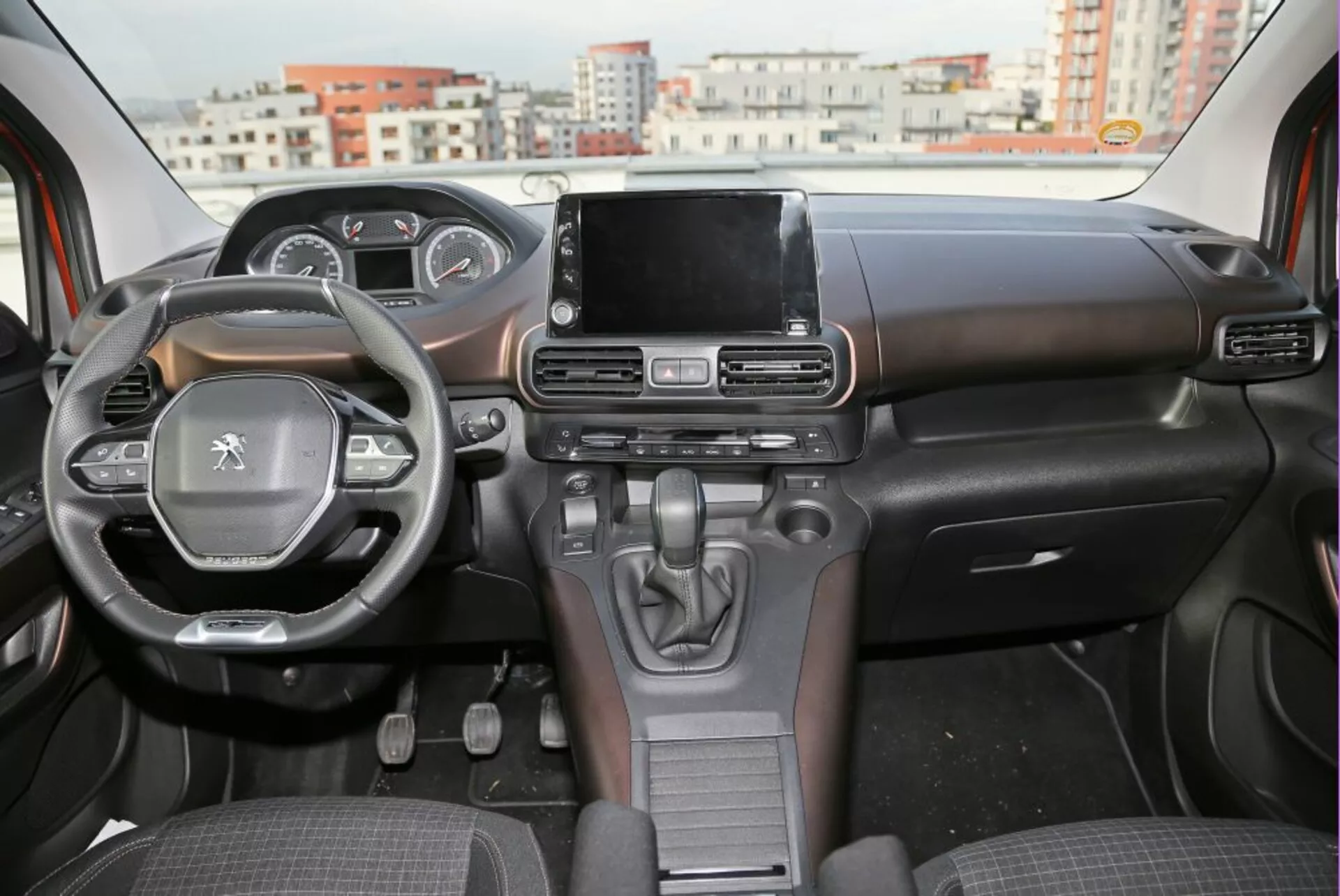 Vista interna di una Peugeot 3008 del 2016 che mostra il cruscotto, il volante con comandi integrati e il touchscreen dell'infotainment centrale dalla prospettiva del sedile posteriore