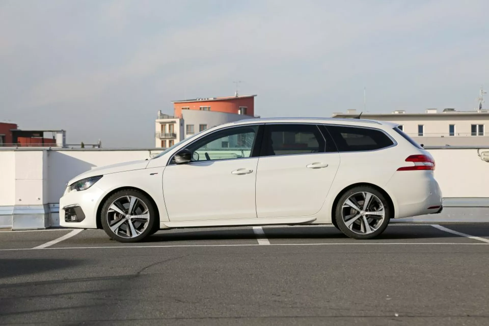 Station wagon Peugeot 3008 bianca del 2016 parcheggiata sull'asfalto, vista laterale che mostra fari eleganti, cerchi in lega a più razze, specchietti laterali color carrozzeria e cinque porte