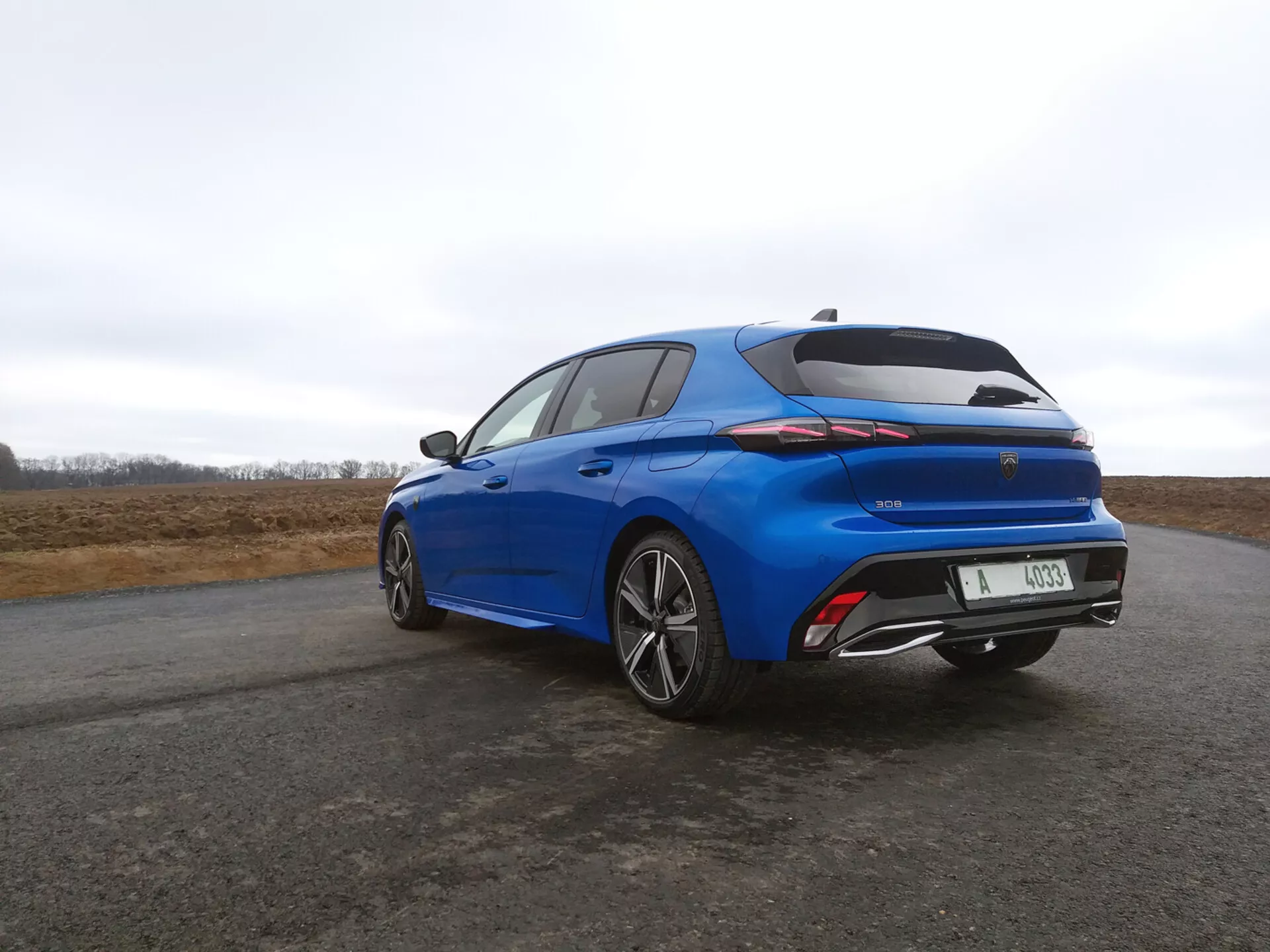 Peugeot 308 hatchback 2022 in blu vibrante, vista a tre quarti posteriore che mette in evidenza fanali posteriori LED, spoiler integrato e cerchi in lega a più razze su sfondo di cielo coperto.