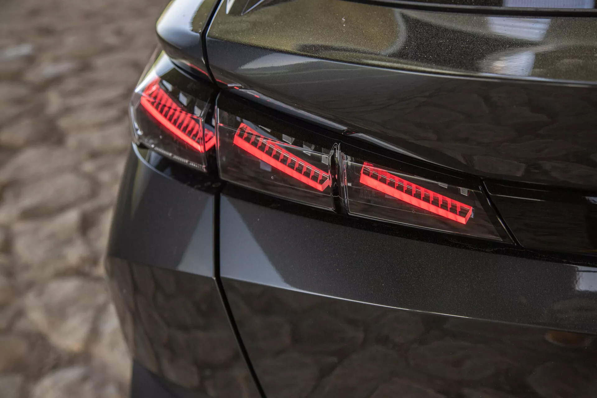 Vista ravvicinata delle luci posteriori nere lucide della Peugeot 408 del 2023, con elementi LED moderni e accenti di design eleganti catturati da un angolo elevato