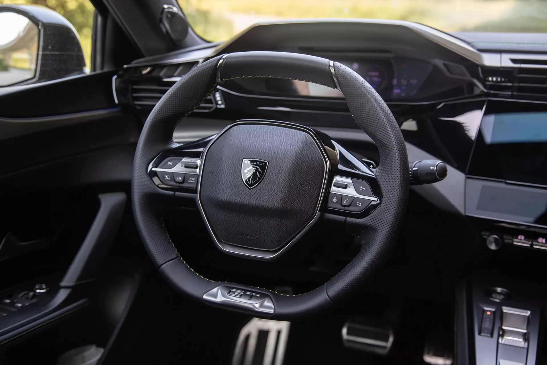Interno della Peugeot 408 del 2023 con volante moderno multifunzione con logo di marca, cruscotto digitale sullo sfondo e console centrale parzialmente visibile con sistema di infotainment