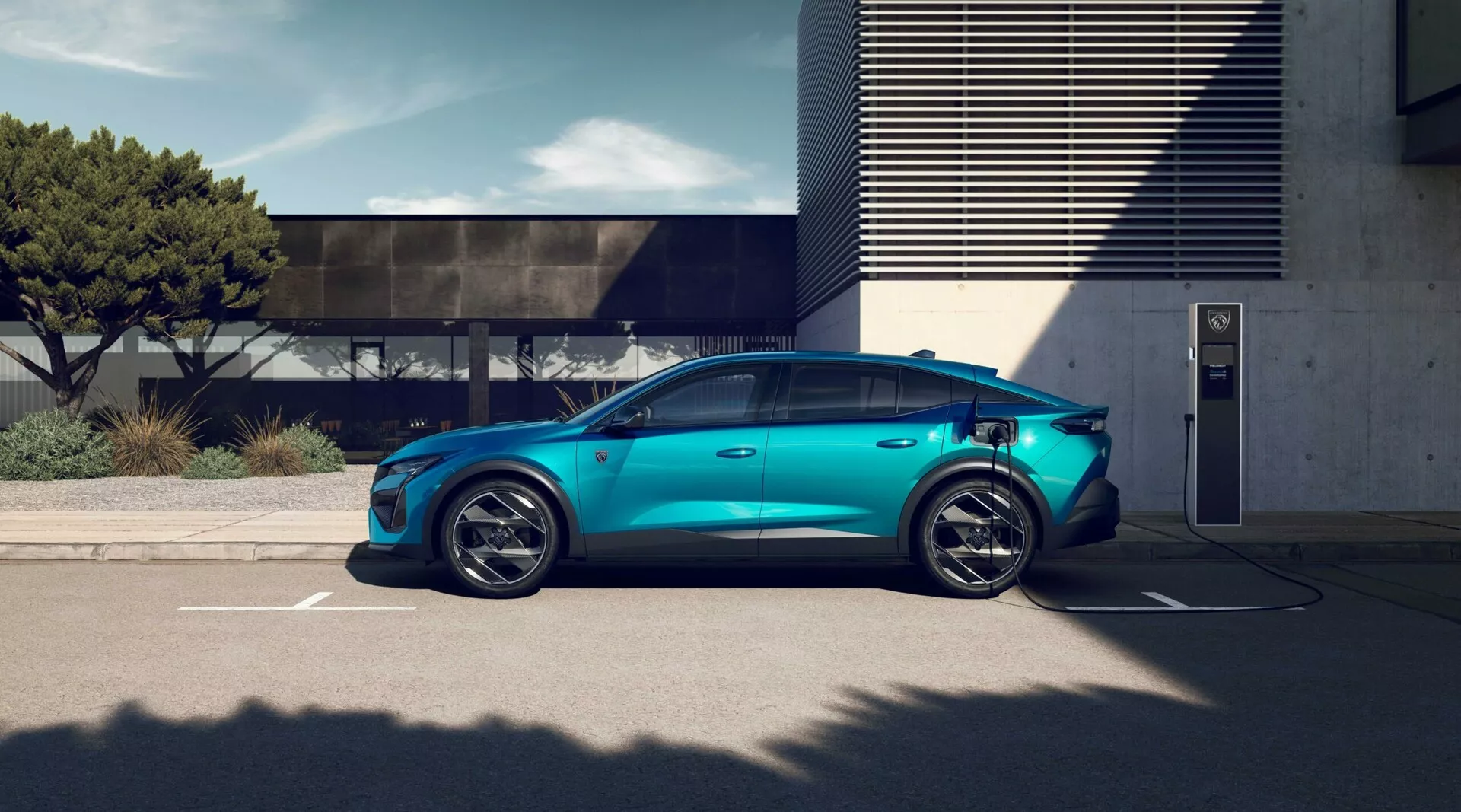 Veicolo elettrico Peugeot 408 del 2023 in blu metallizzato parcheggiato presso stazione di ricarica esterna, con ruote in lega a cinque razze sportive, silhouette aerodinamica, maniglie delle porte a filo, porta di ricarica visibile, specchietti laterali convenzionali, vetri oscurati per la privacy e tetto panoramico sotto condizioni di luce diurna luminosa con architettura moderna sullo sfondo
