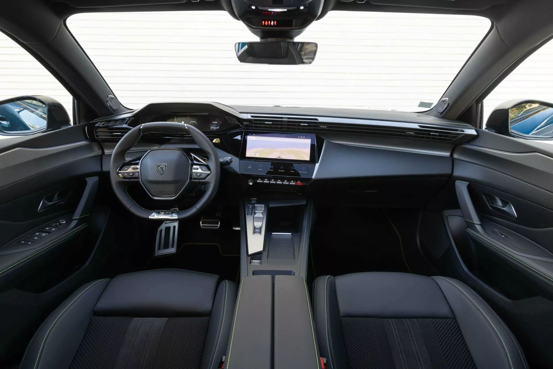 Vista interna della Peugeot 408 2023 dalla zona dei sedili posteriori che evidenzia il cruscotto, il volante multifunzione con emblema del marchio e il sistema di infotainment avanzato