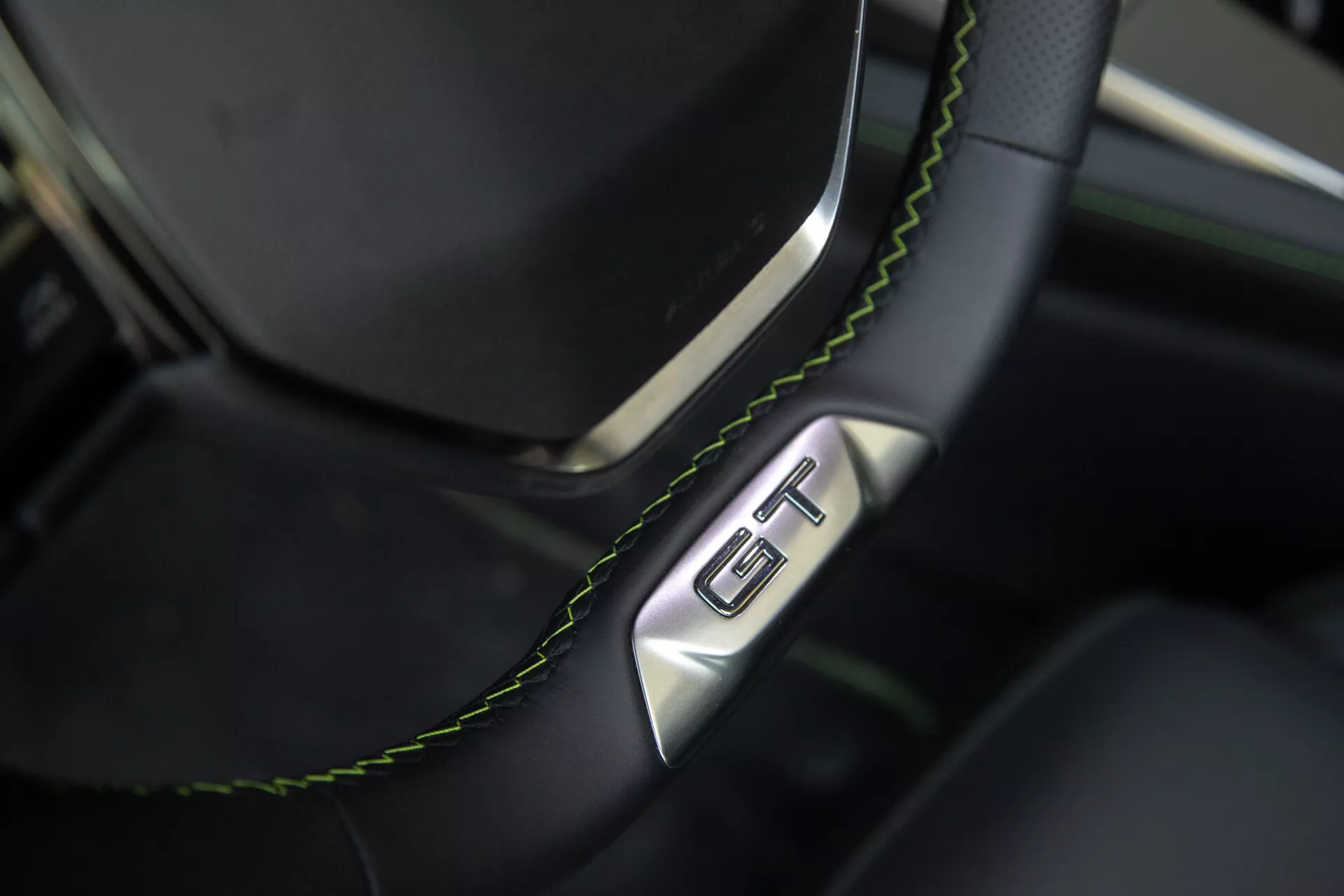 Vista ravvicinata della sezione volante e cruscotto della Peugeot 408 2023, con volante in pelle nera con cuciture verdi e distintivo GT, evidenziando lusso e sportività