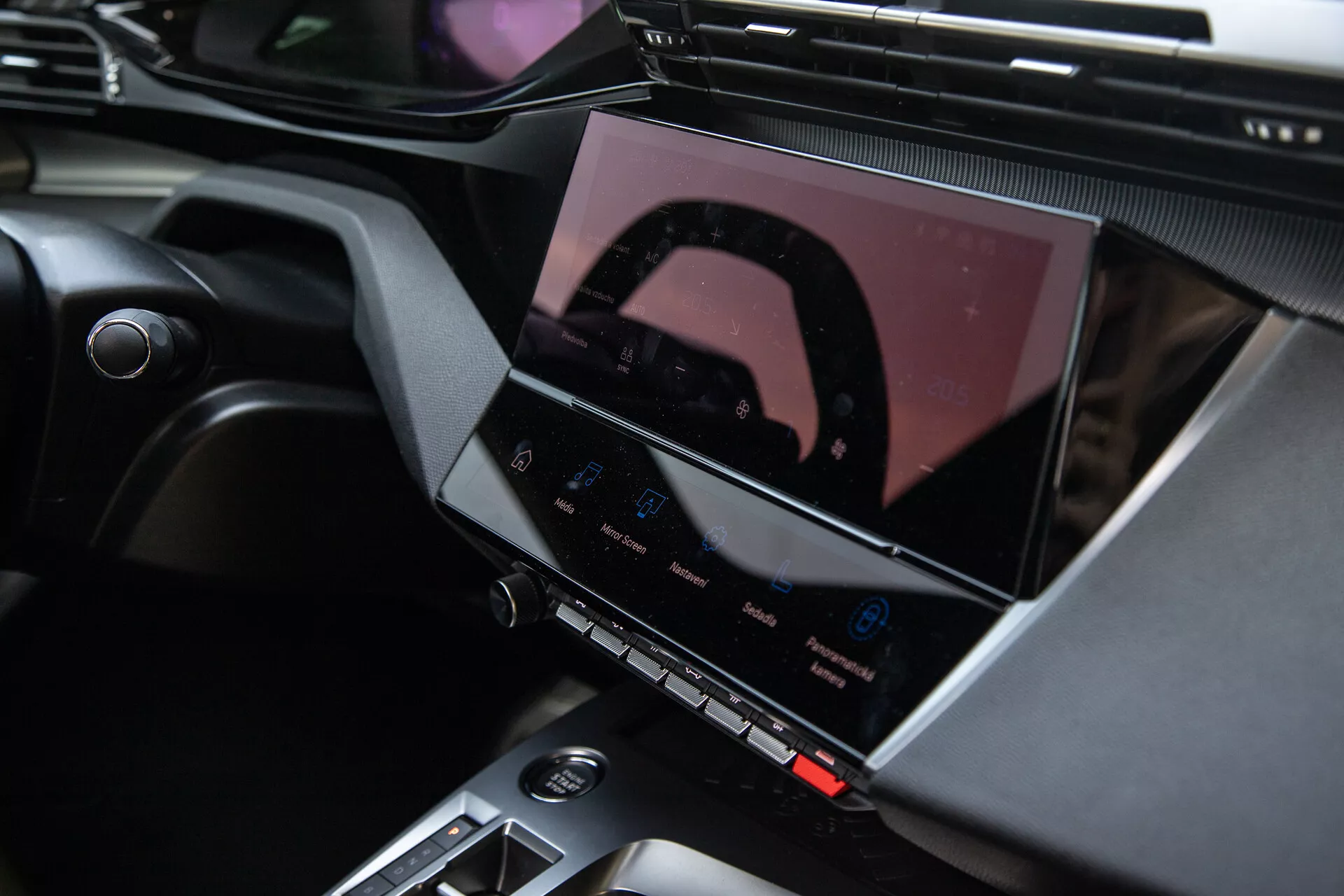 Interni della Peugeot 408 2023 con console centrale e avanzato sistema di infotainment con display touchscreen, pulsanti per il controllo del clima e raffinati accenti di design
