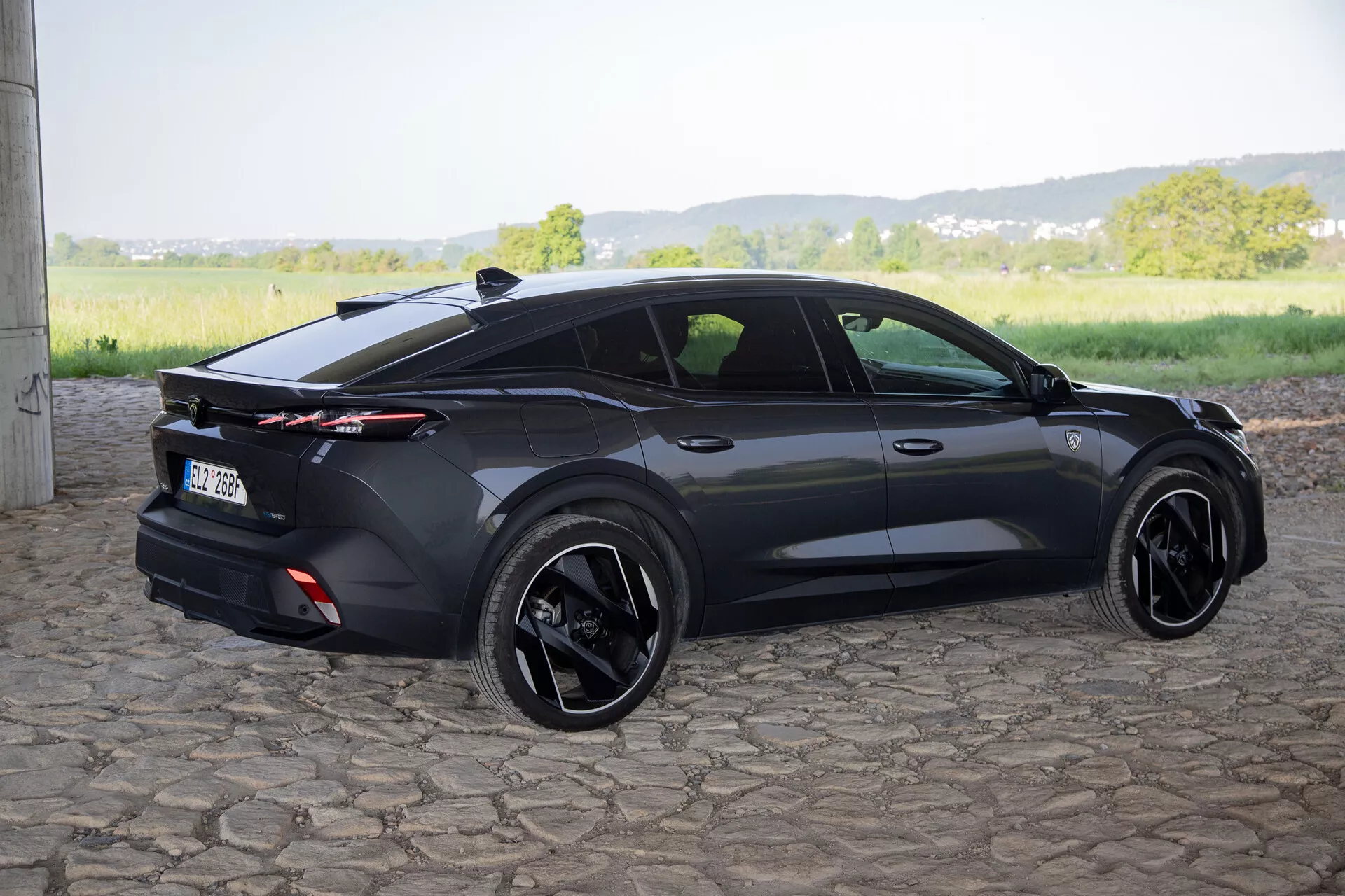 Peugeot 408 del 2023 ripresa da un angolo posteriore di tre quarti che evidenzia il suo design sportivo hatchback, spoiler posteriore integrato con luci posteriori a tutta lunghezza, ruote in lega nere, e caratteristiche contemporanee come maniglie delle porte a filo e specchietti laterali con indicatori di direzione, alla luce naturale del giorno