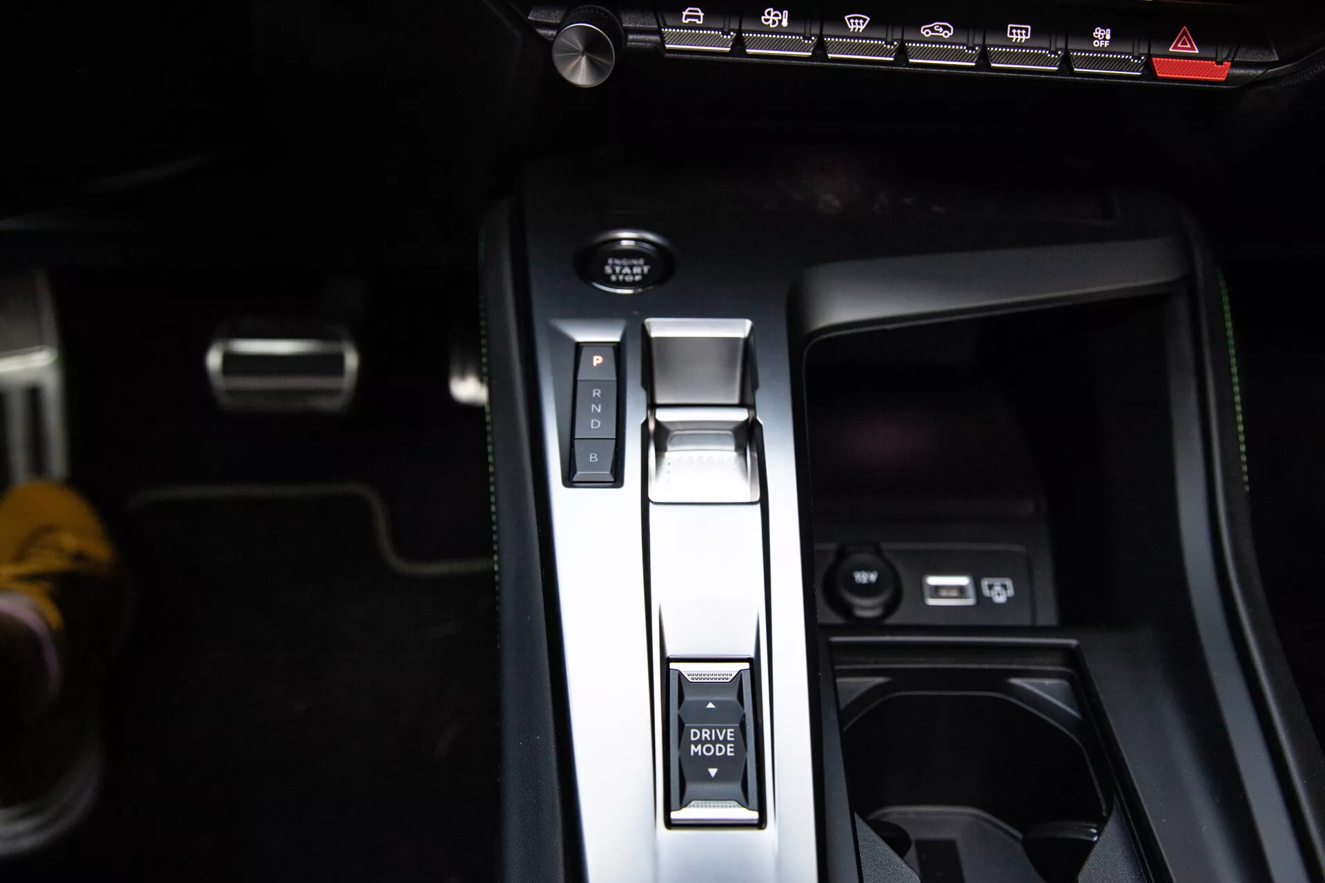 Vista ravvicinata della console centrale della Peugeot 408 2023 con leva del cambio in posizione Parcheggio, pulsante MODALITÀ DI GUIDA, freno di parcheggio elettronico e porte USB, mettendo in mostra un design interno moderno.