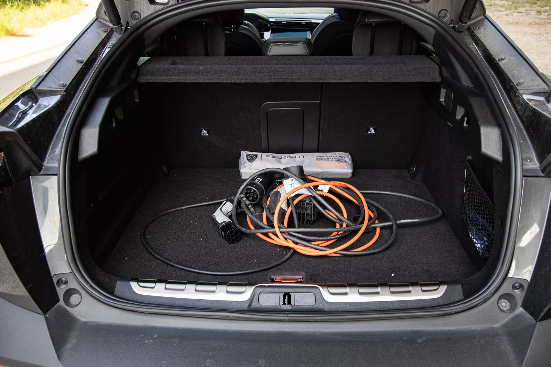 Vista interna del bagagliaio della Peugeot 408 2023 che mostra un design spazioso e un cavo di ricarica per veicoli elettrici, evidenziando la tecnologia EV e la qualità costruttiva moderna.