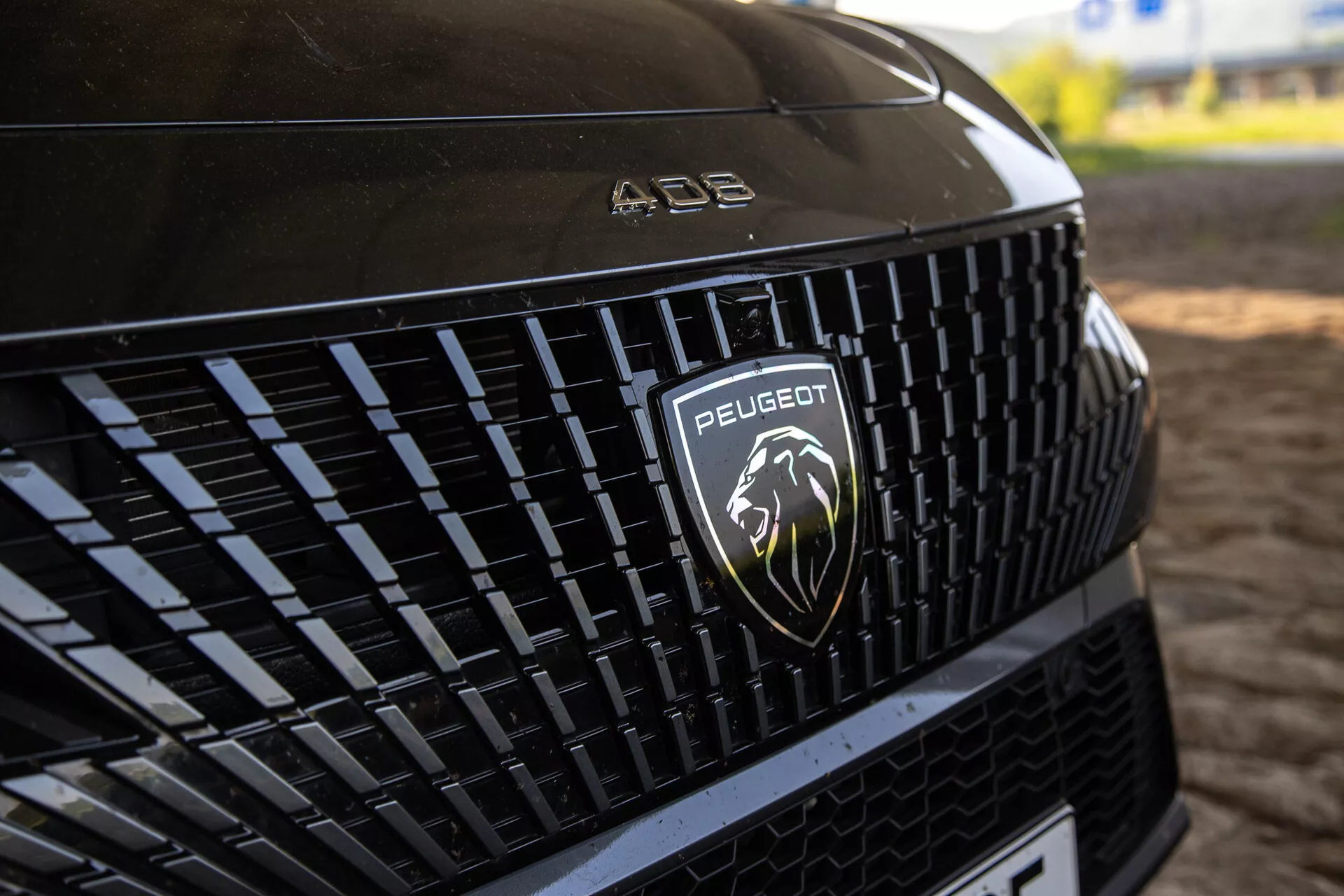 Vista dettagliata della griglia frontale della Peugeot 408 2023 che mostra il motivo intricato e il logo del leone argentato, sotto l'illuminazione naturale
