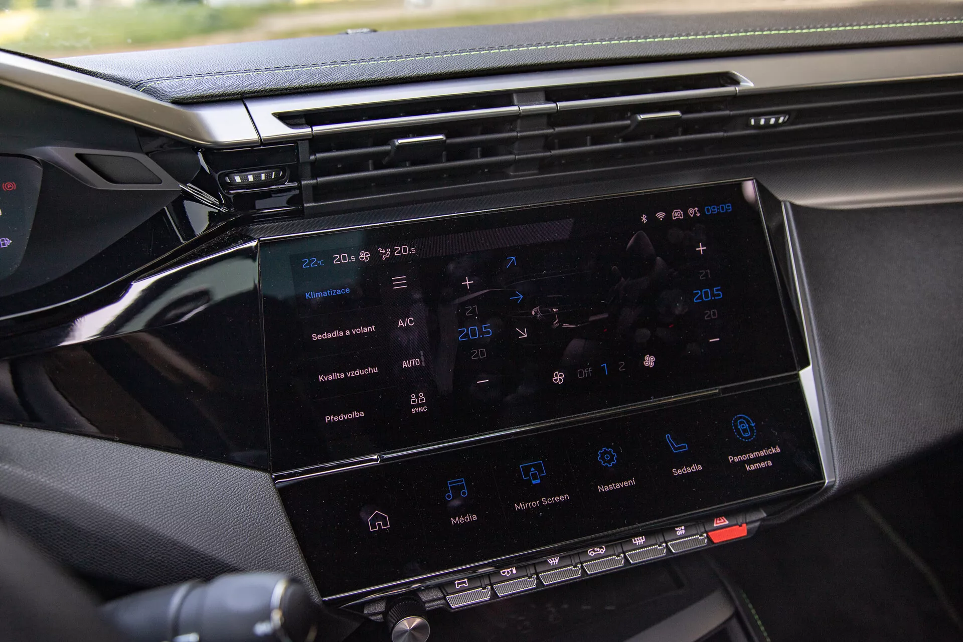 Primo piano del sistema d'infotainment della Peugeot 408 2023 che mostra un display a schermo tattile da 8-10 pollici con navigazione, controllo del clima, icone di riproduzione dei media e scorcio del cruscotto, scattata dal lato passeggero