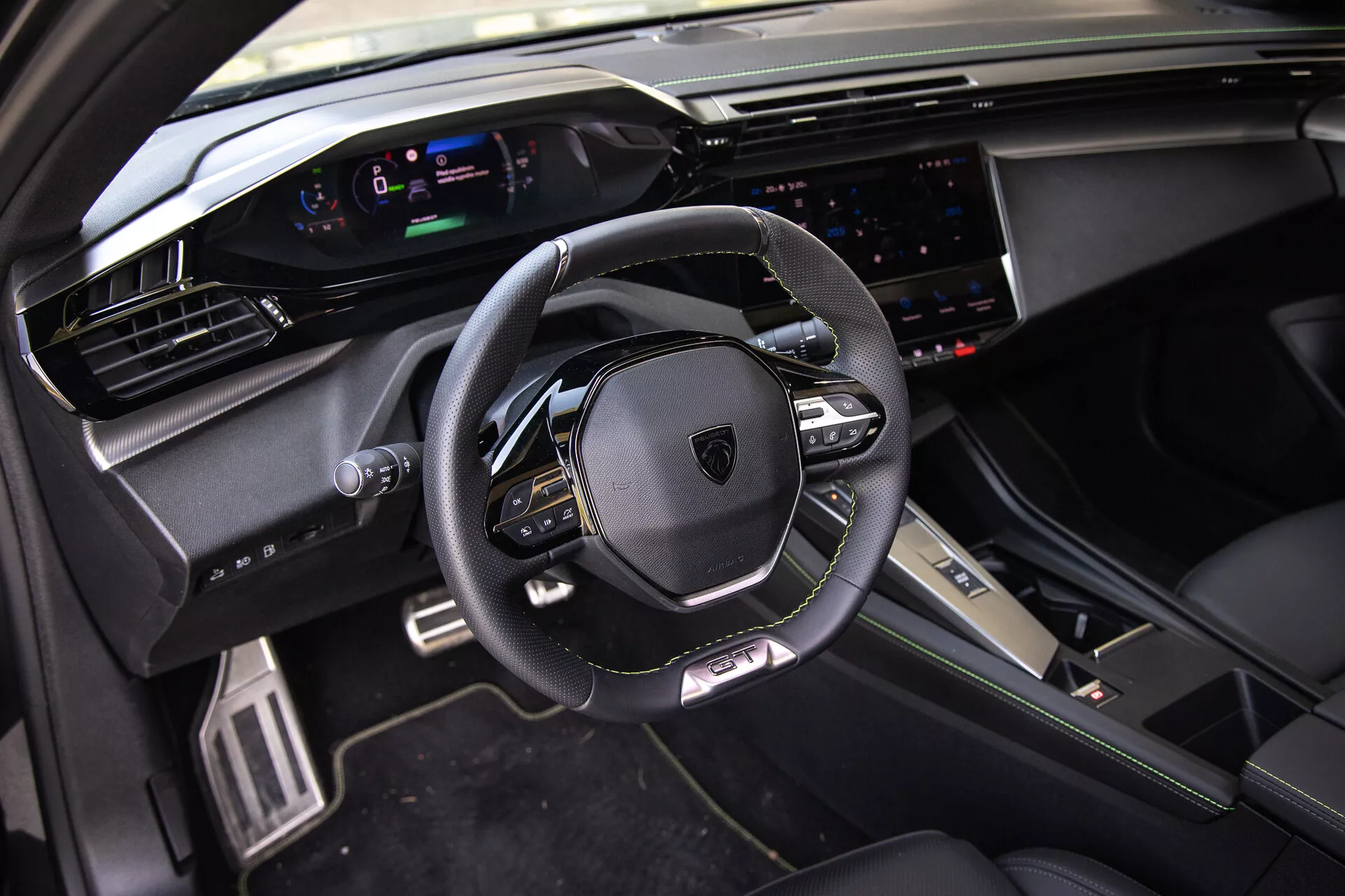 Interni del Peugeot 408 2023 che mostrano un volante multifunzionale rivestito in pelle, un cruscotto digitale, un ampio sistema di infotainment touchscreen e elementi di design sportivo premium alla luce naturale dalla prospettiva del passeggero anteriore.