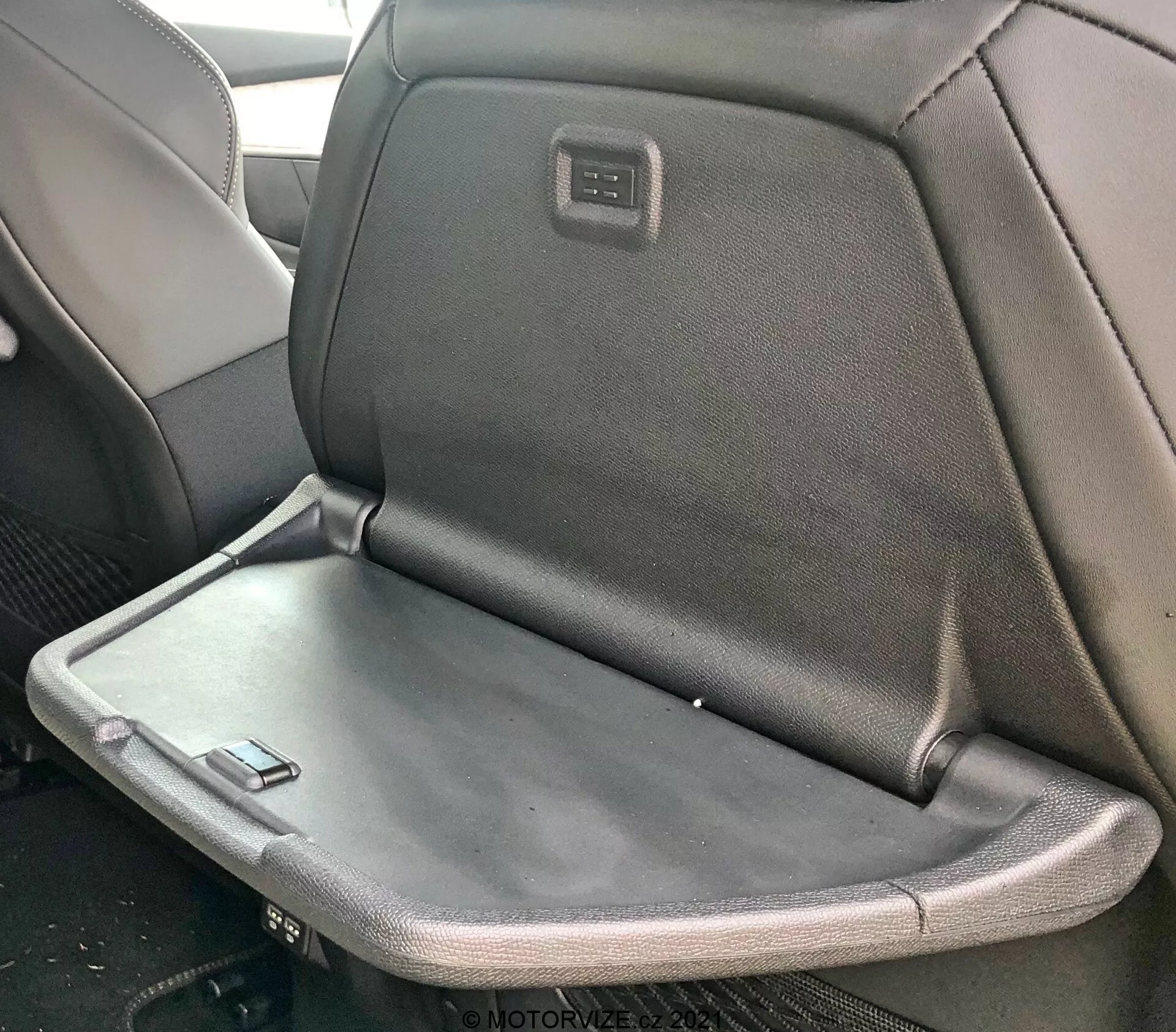 Vista interna di una Peugeot 5008 2021 con il sedile posteriore che presenta un bracciolo pieghevole o tavolino, con tappezzeria mista in tessuto e pelle e uno schermo o pannello di controllo integrato nella parte posteriore del poggiatesta del sedile anteriore.