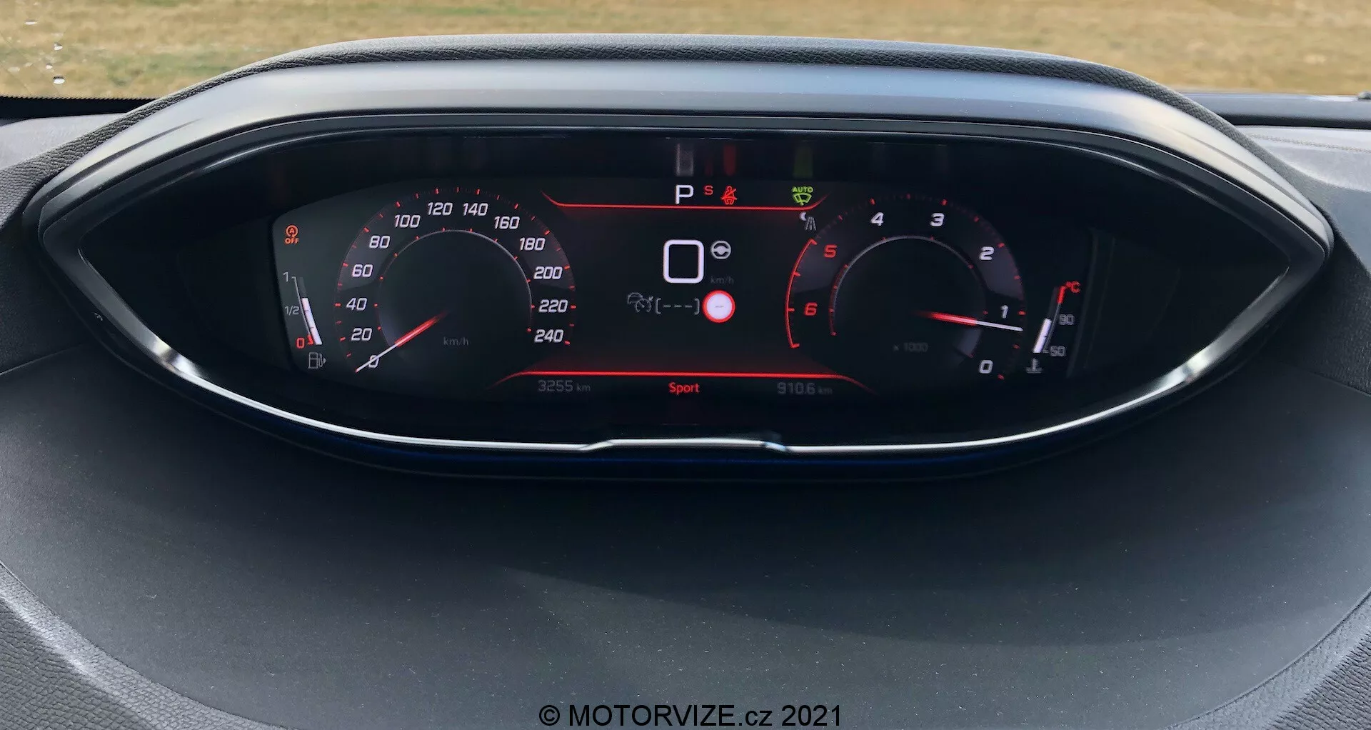 Vista ravvicinata del cruscotto del Peugeot 5008 del 2021, con display digitale e indicatori in stile analogico. Il display mostra tachimetro, contagiri, selezione marcia e vari indicatori del veicolo come avvertenze di sicurezza e modalità di guida. L'auto è ferma con modalità di guida 'Sport' attiva.