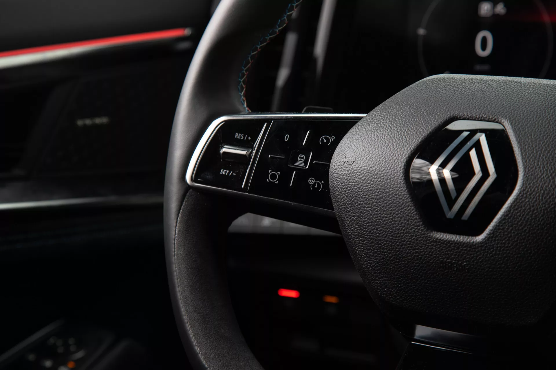 Vista interna del Renault Austral 2022 che evidenzia i comandi sul volante e l’emblema, incluse le funzioni dei pulsanti illuminati per volume, chiamate, comandi vocali e navigazione dell'infotainment, dalla prospettiva del sedile del guidatore.