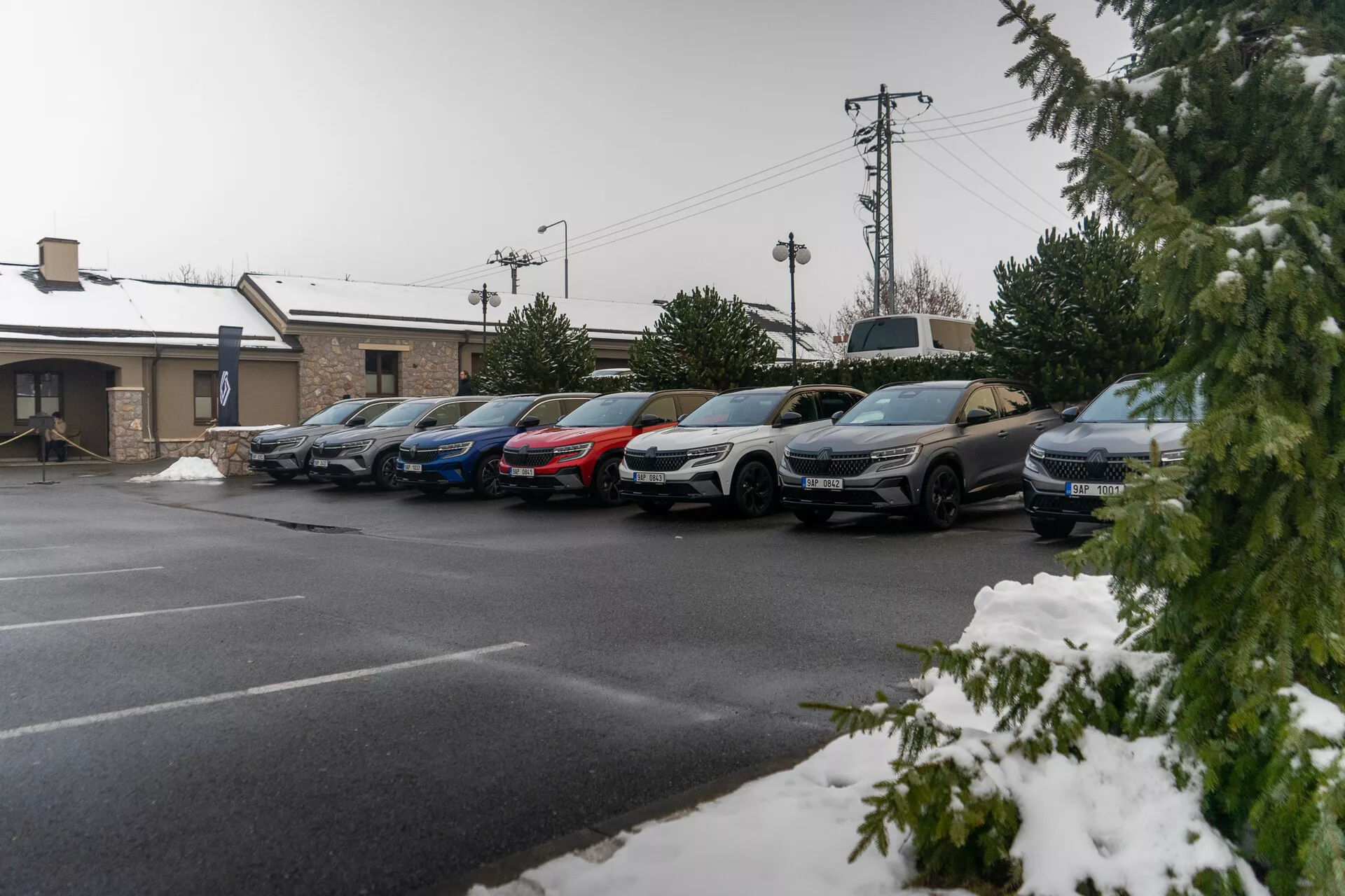 Serie di auto parcheggiate, tra cui berline e SUV, sotto una leggera nevicata, indicando tempo freddo, con profili laterali visibili inclusi porte, specchietti laterali e ruote, scattata da un angolo elevato del marciapiede