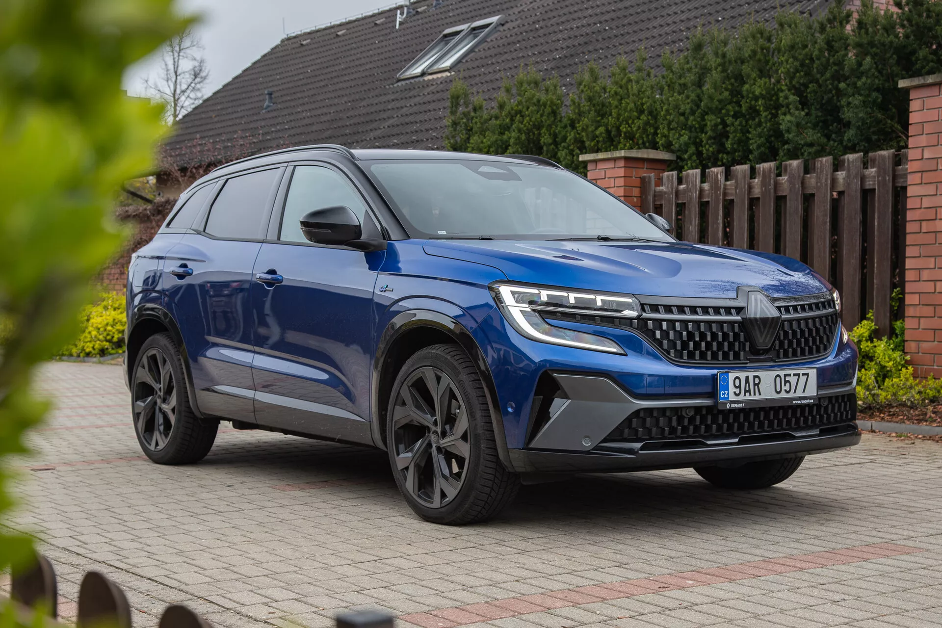 SUV moderno Renault Austral 2022 mostrato in prospettiva frontale a tre quarti che evidenzia fari LED, una griglia prominente, ruote in lega alla moda e carrozzeria dinamica con finitura vernice metallizzata, fotografato da un angolo basso per sottolineare la sua statura e le caratteristiche di design su uno sfondo residenziale.