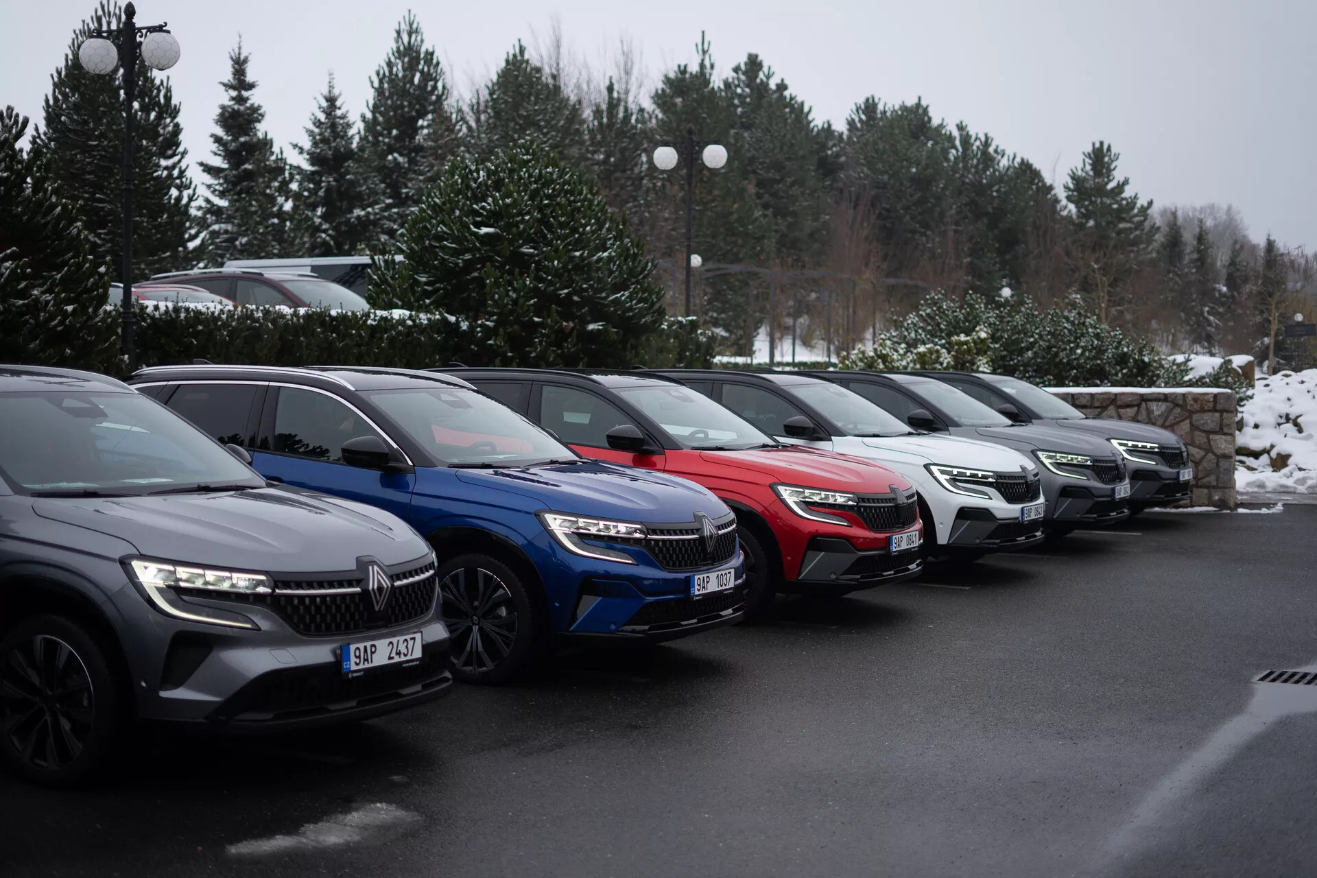 Linea di cinque auto Renault Austral 2022 parcheggiate a 45 gradi in un parcheggio invernale, mostrando modelli in grigio scuro, blu, rosso, argento e grigio, con fari LED e griglie frontali moderne