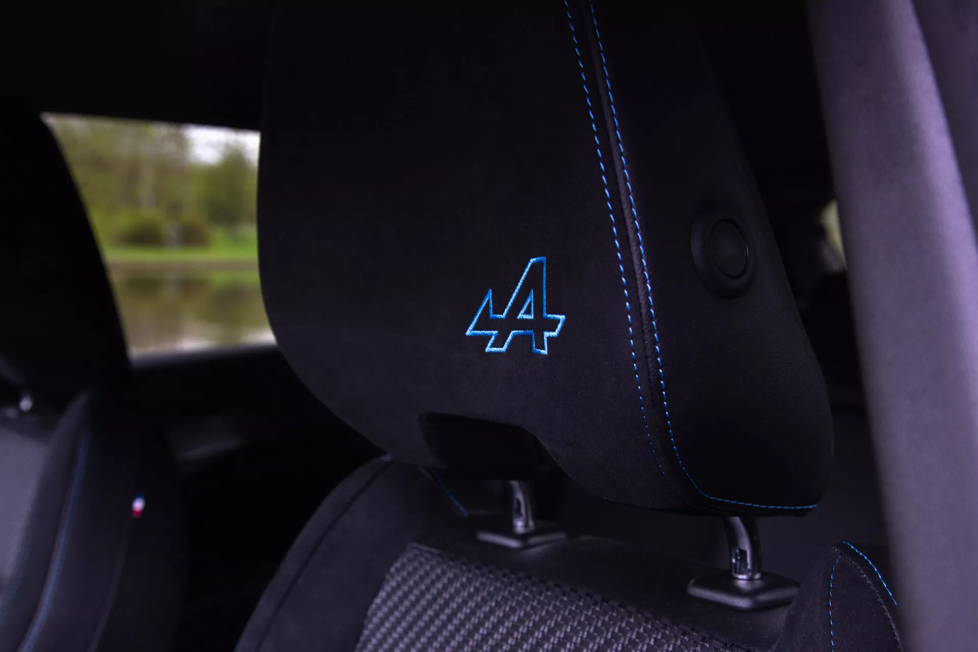 Vista ravvicinata dell'interno della Renault Austral 2022 che mostra il sedile del conducente in tessuto nero con cuciture blu distintive e logo stilizzato 'A' sul poggiatesta, guida per cintura di sicurezza integrata visibile, suggerendo caratteristiche di veicolo moderno e possibilmente sportivo.